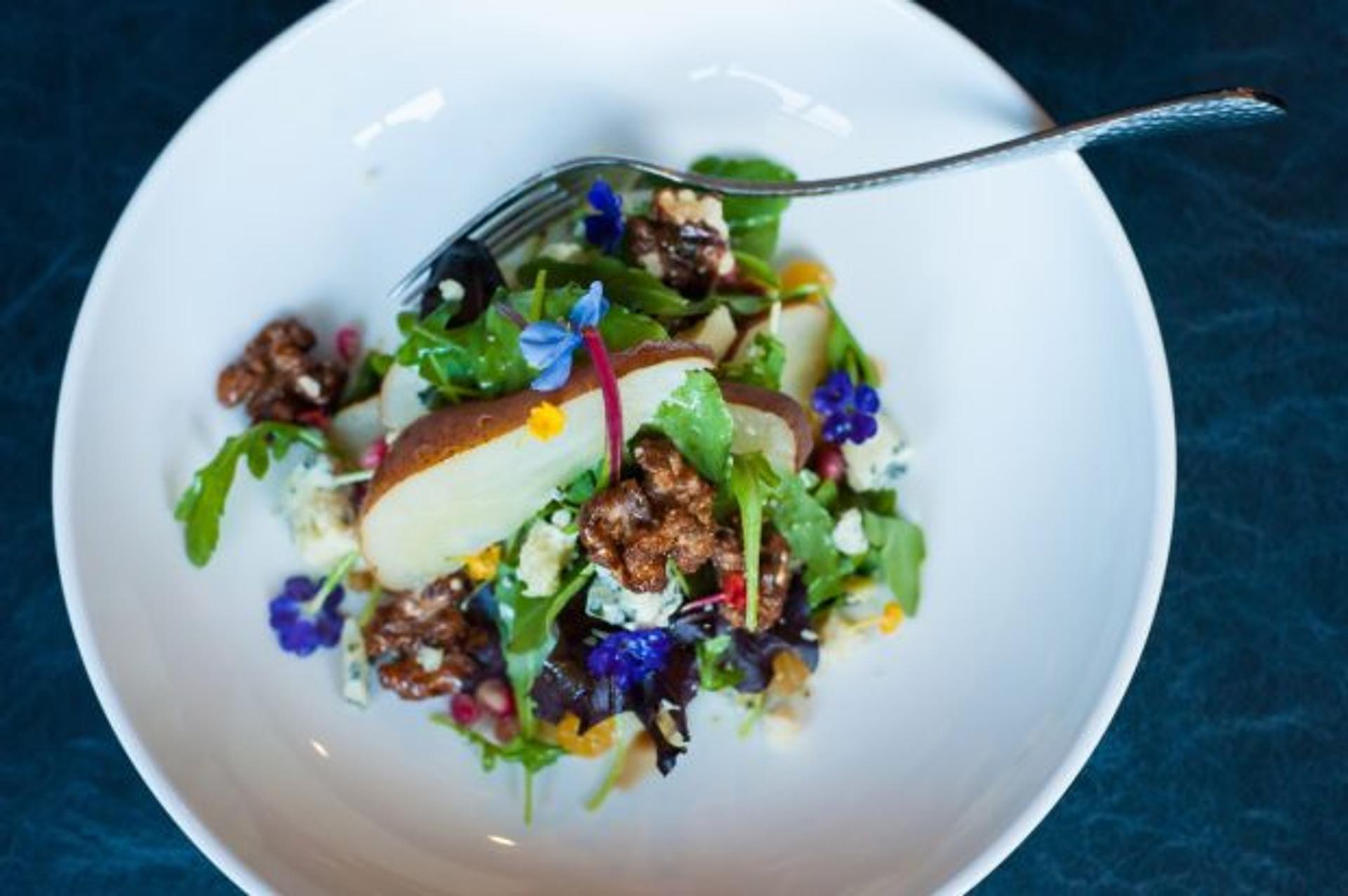 Overhead view of a colorful salad of apples, candied walnuts, microgreens, and edible blue flowers.