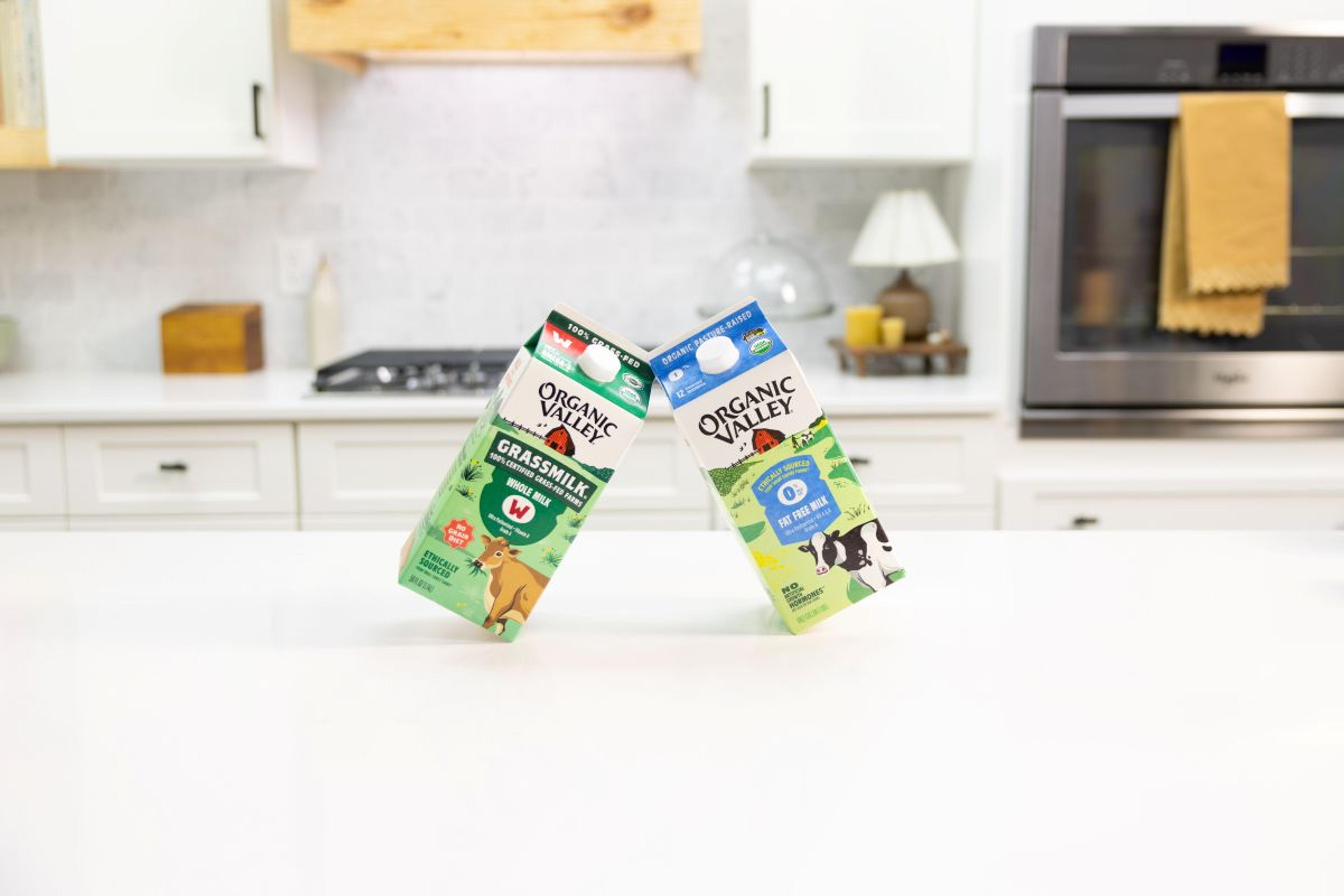 A carton of organic whole milk balanced on a carton of skim dairy milk on a kitchen island.