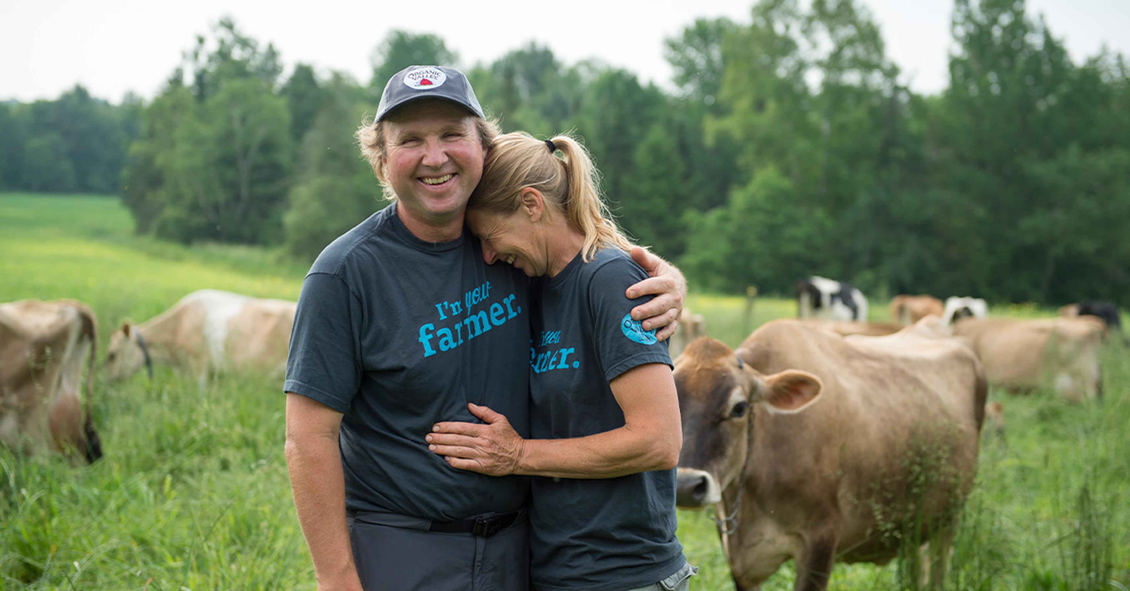 Doug and Linda Hartkopf hug and smile while cows graze in the background.