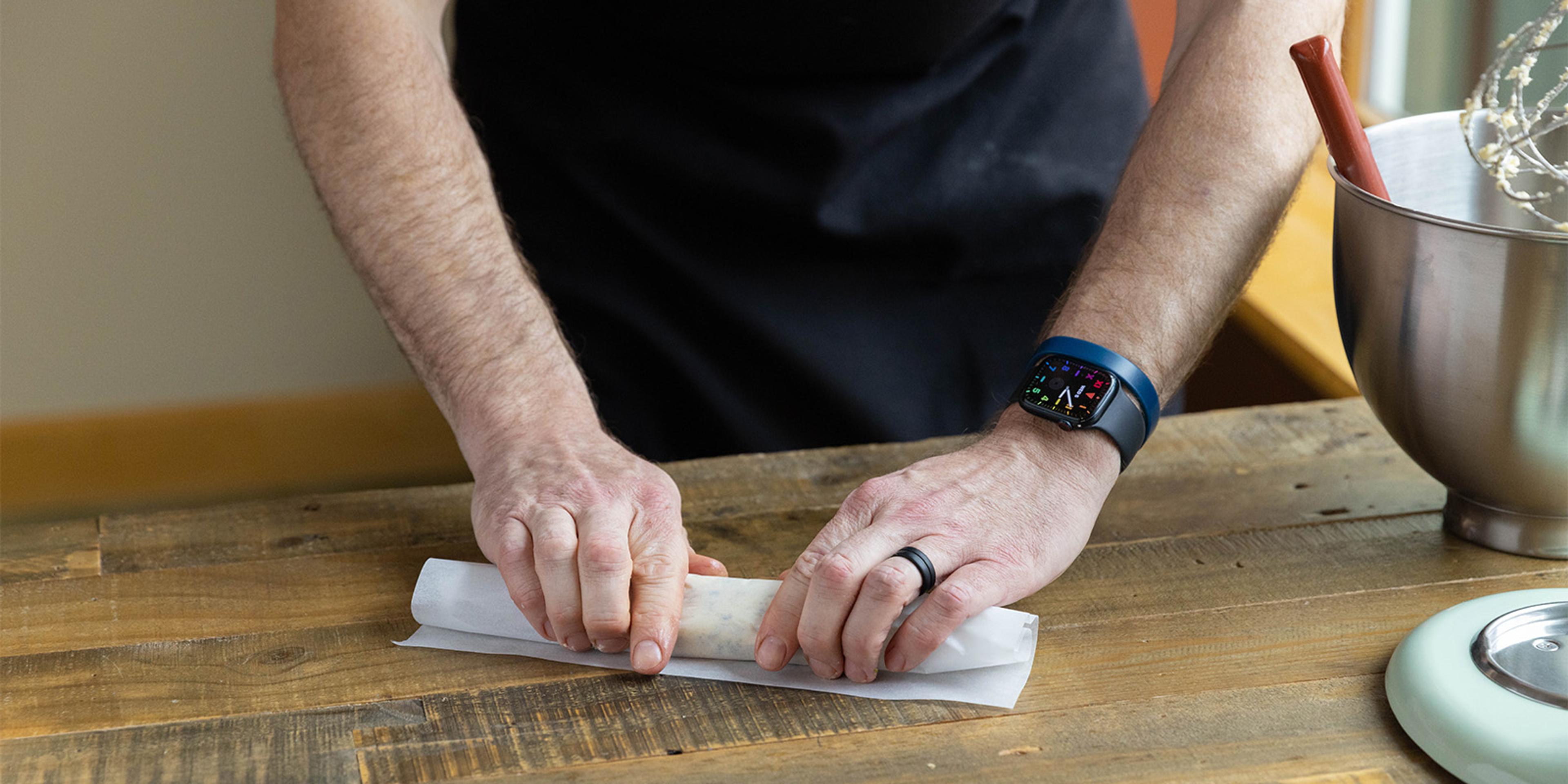 A man rolls butter infused with herbs in parchment paper.