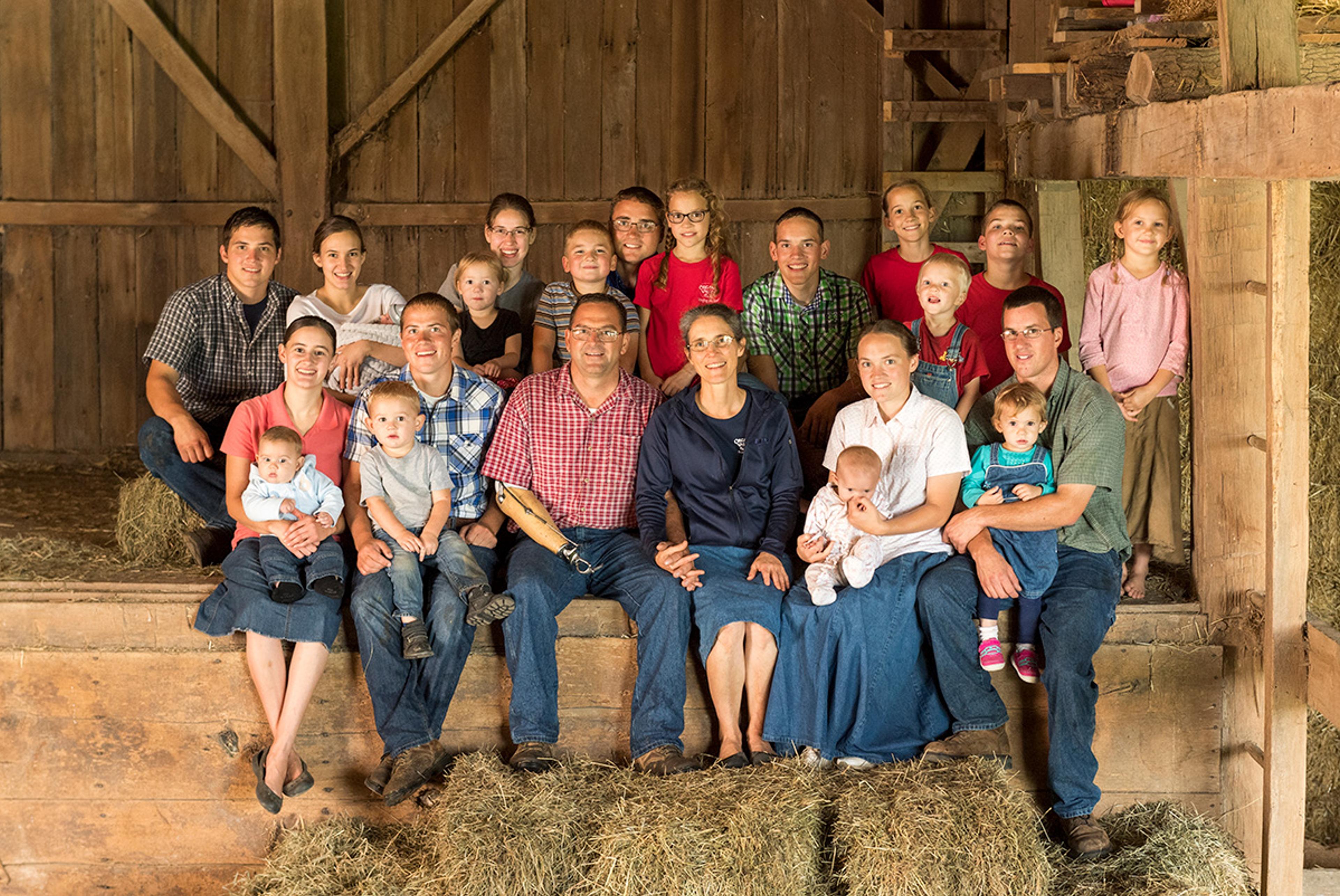 The 23-person Stoller family poses for a portrait in their barn surrounded by hay bales.