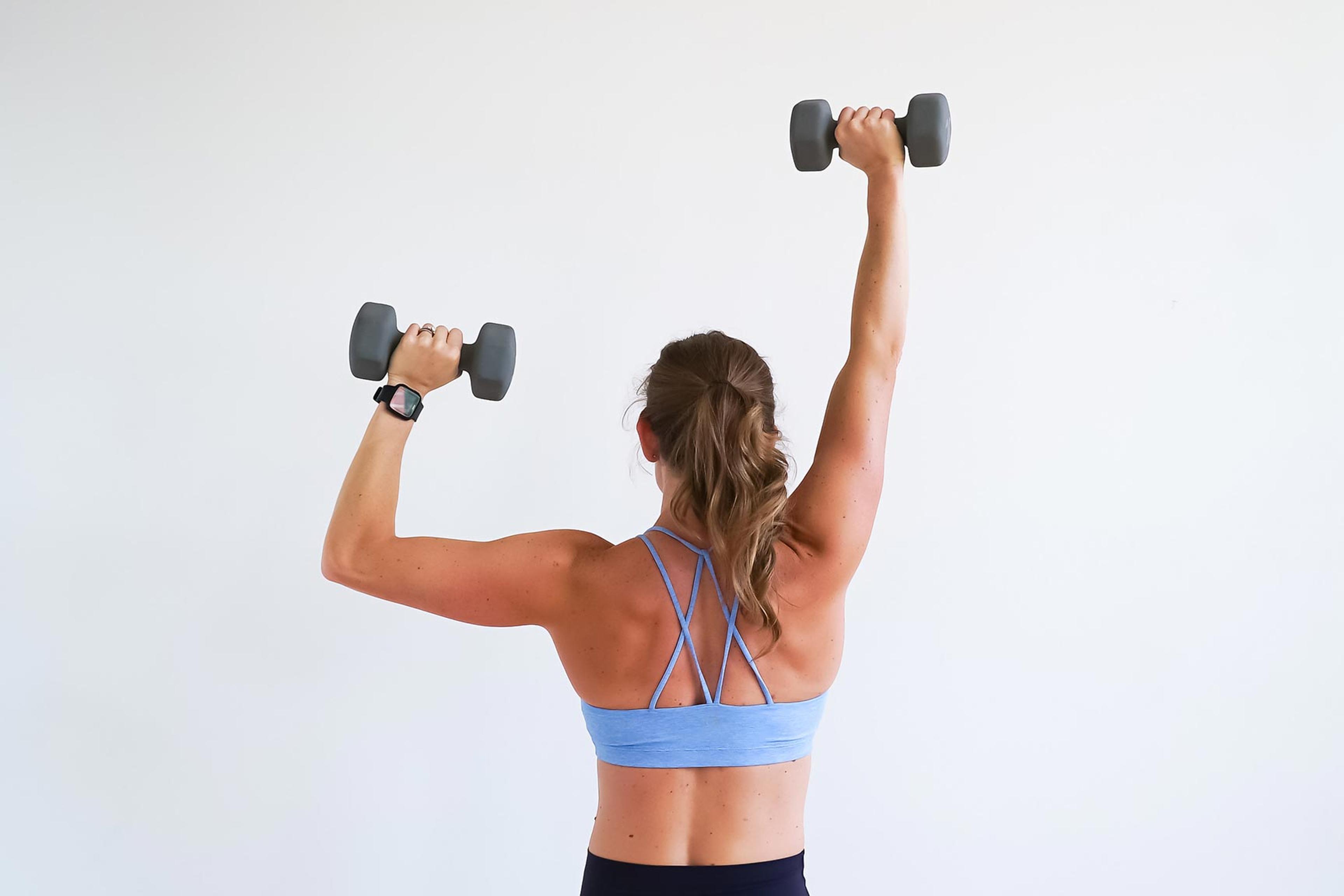 View from behind of a woman doing shoulder press-ups with dumbbells.