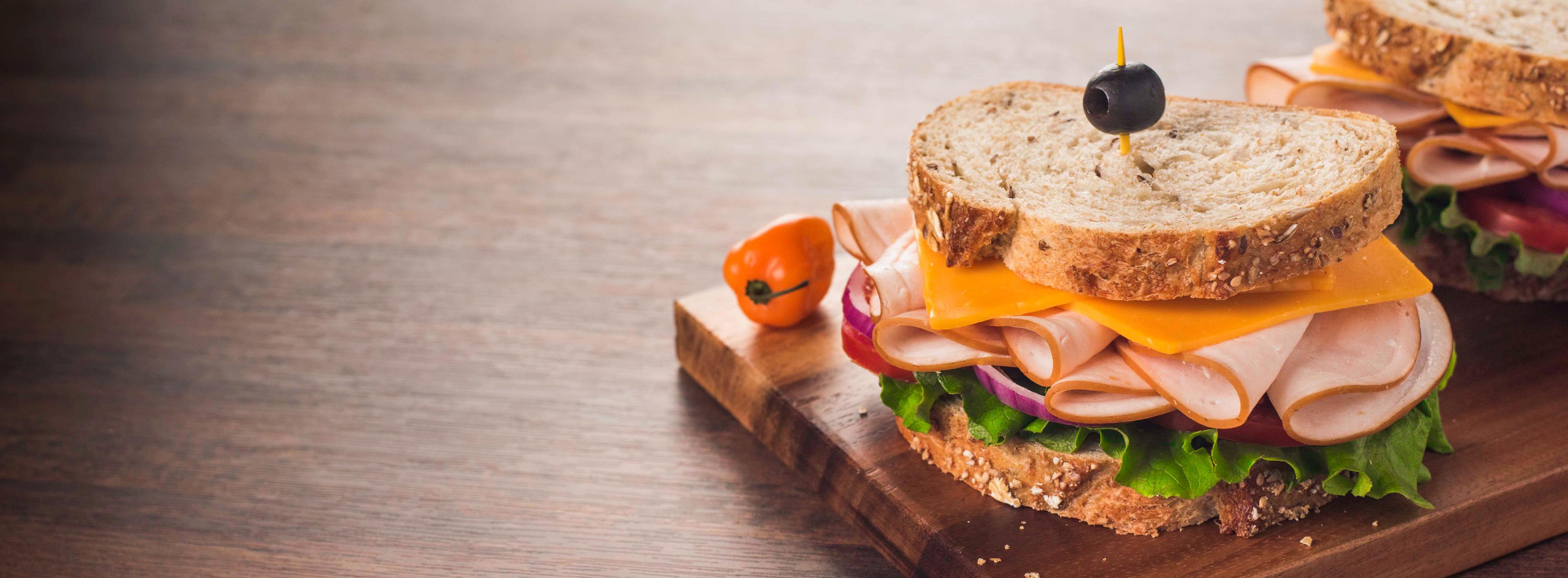 Sandwich on a cutting board with deli slices, cheese and lettuce.