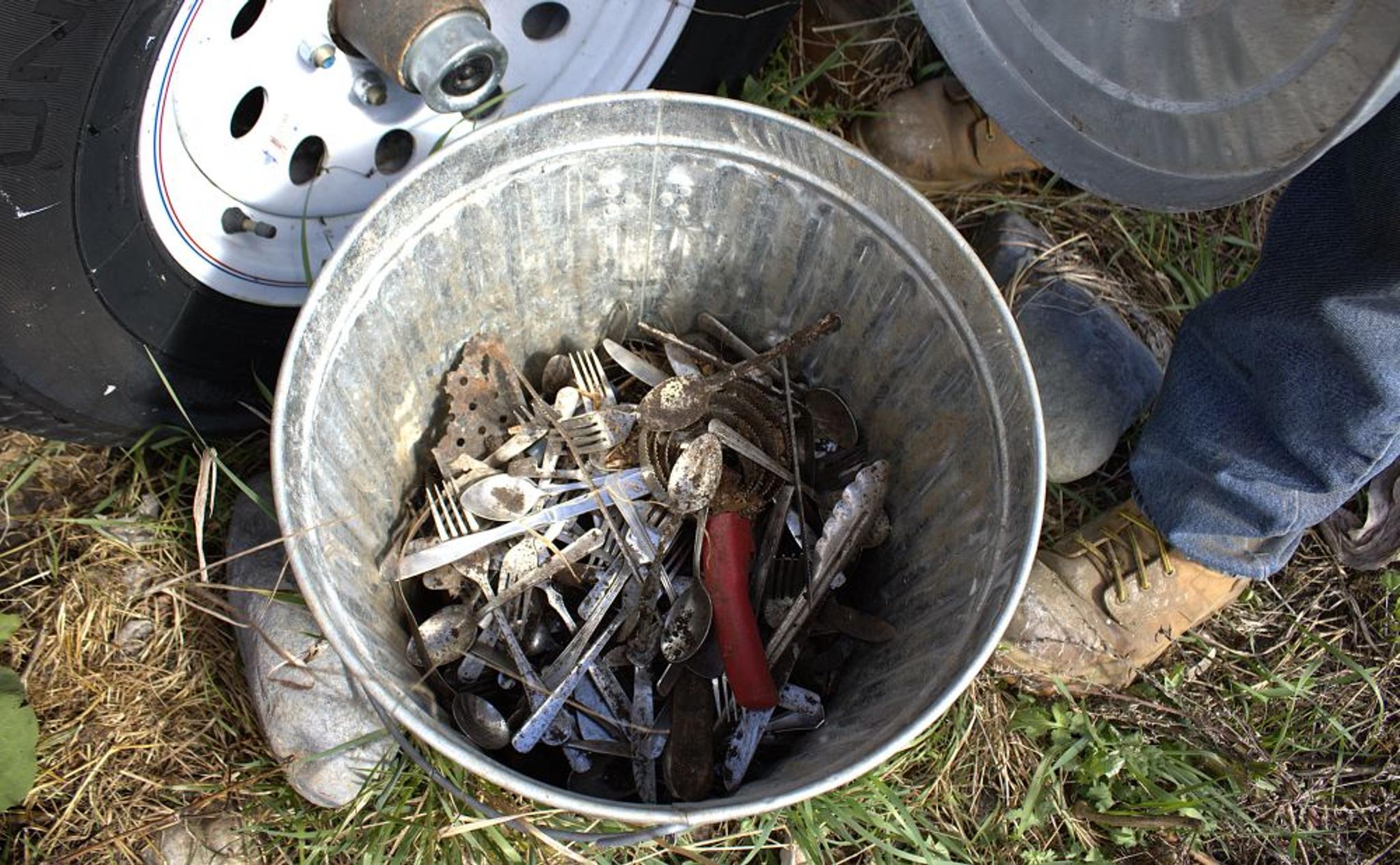 A bucket of kitchen utensils rests on the ground.