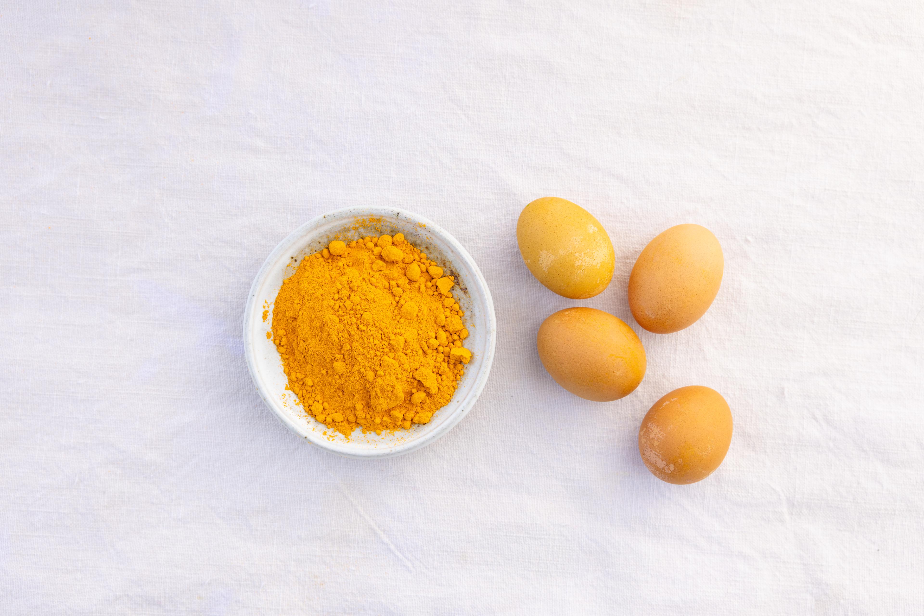 Turmeric powder next to eggs dyed with it.