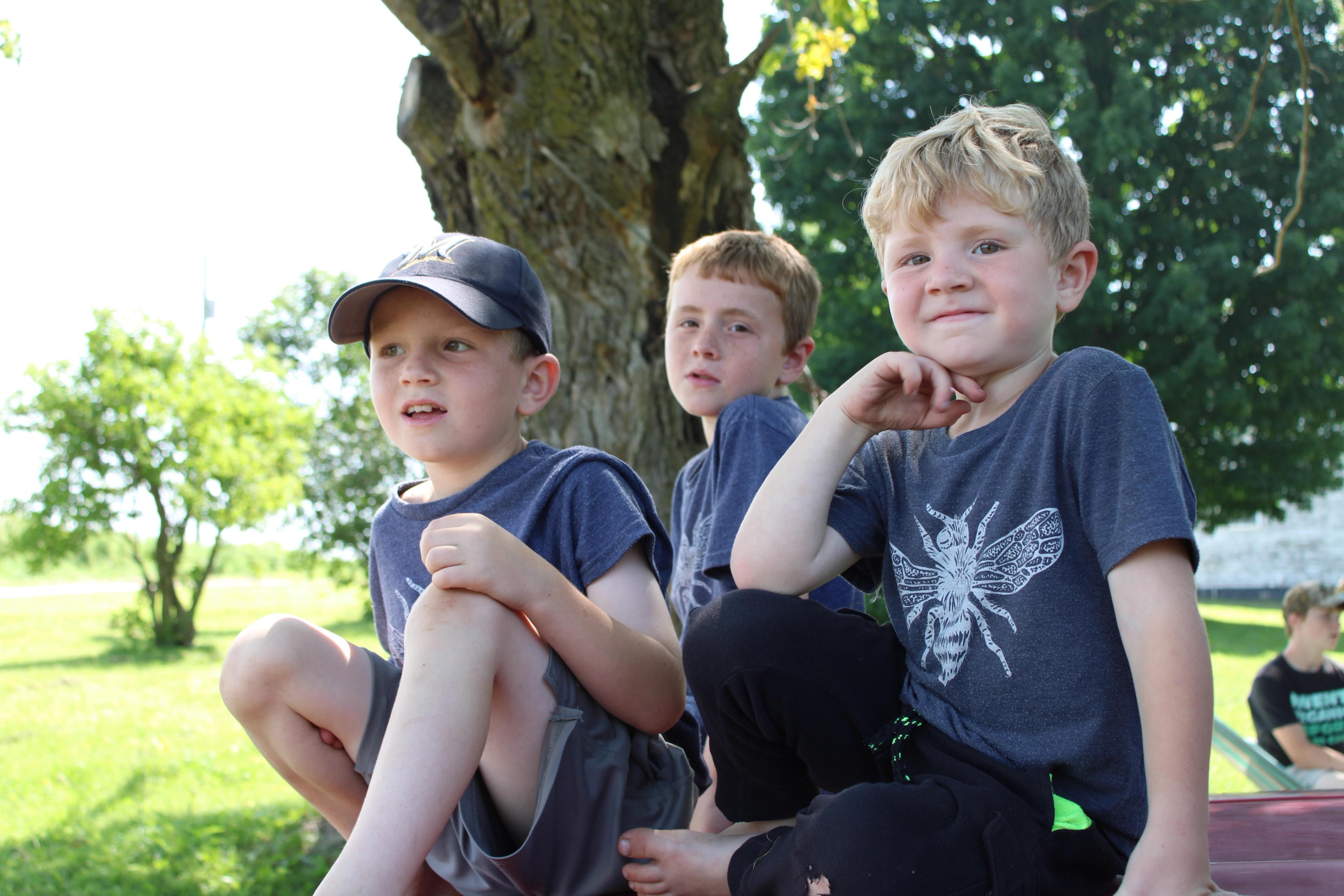 Three boys sit on the hood of a car. 