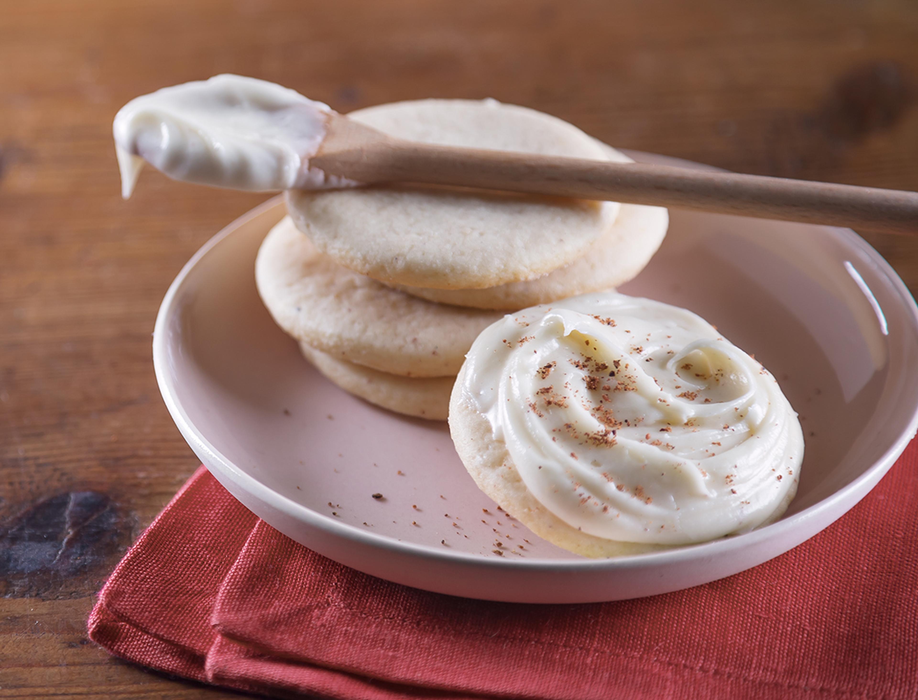 Eggnog sugar cookies with white frosting and a sprinkling of nutmeg on a white plate.