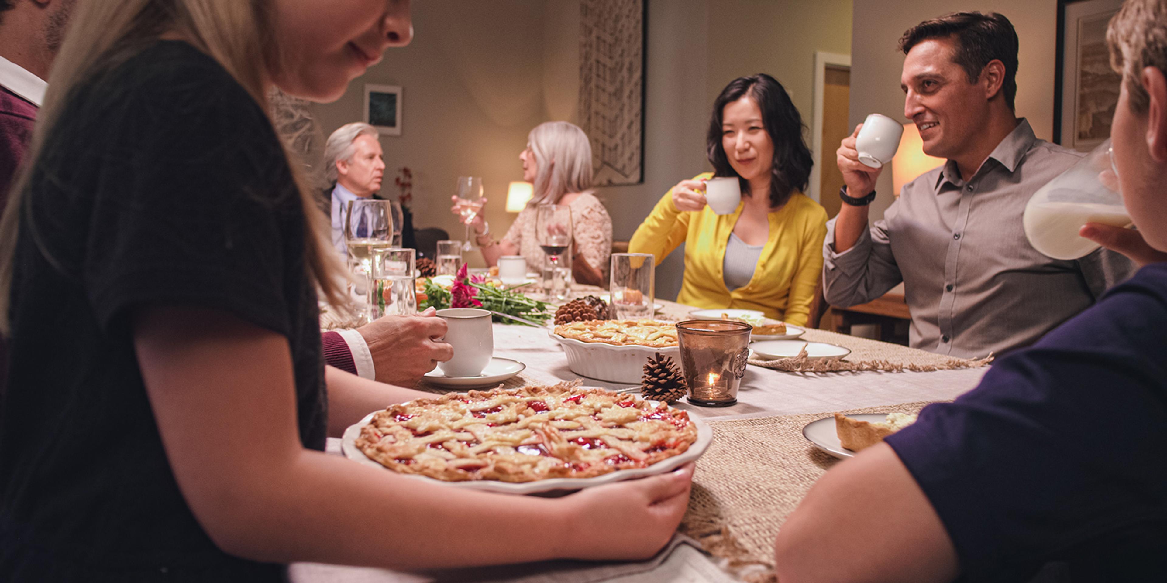 Family sits around a table and serves up an apple pie.