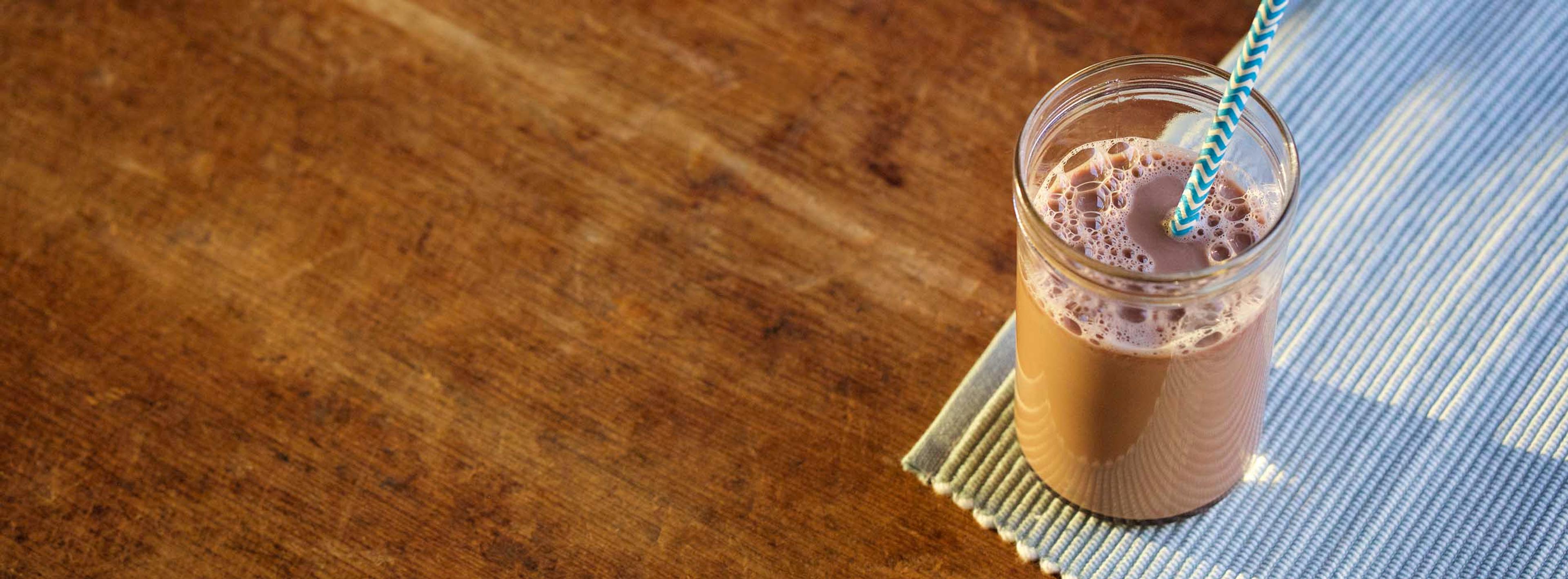 A glass of chocolate milk with a blue straw.