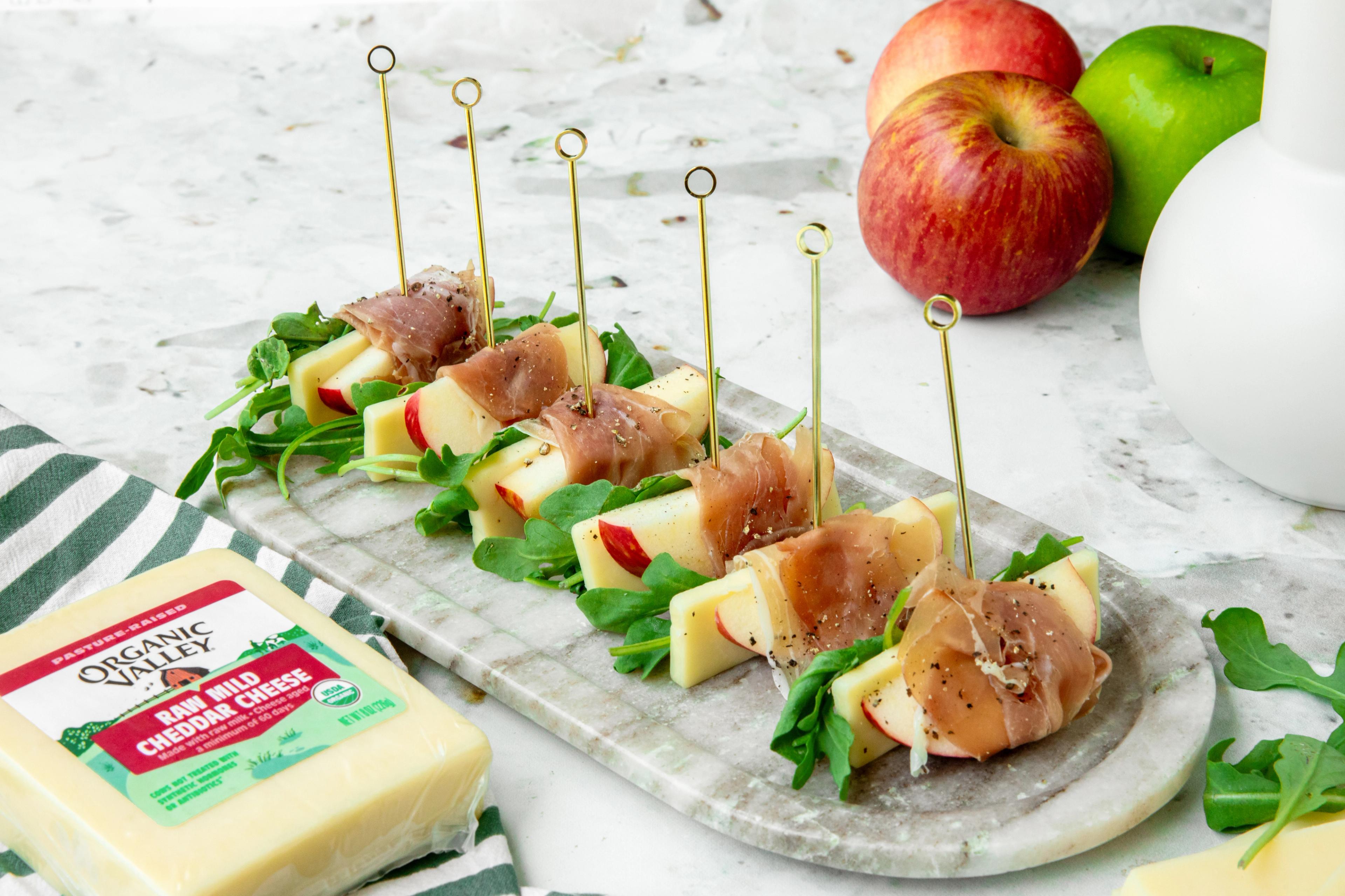 Cheddar apple prosciutto bites on a granite counter next to a block of raw milk cheddar cheese.
