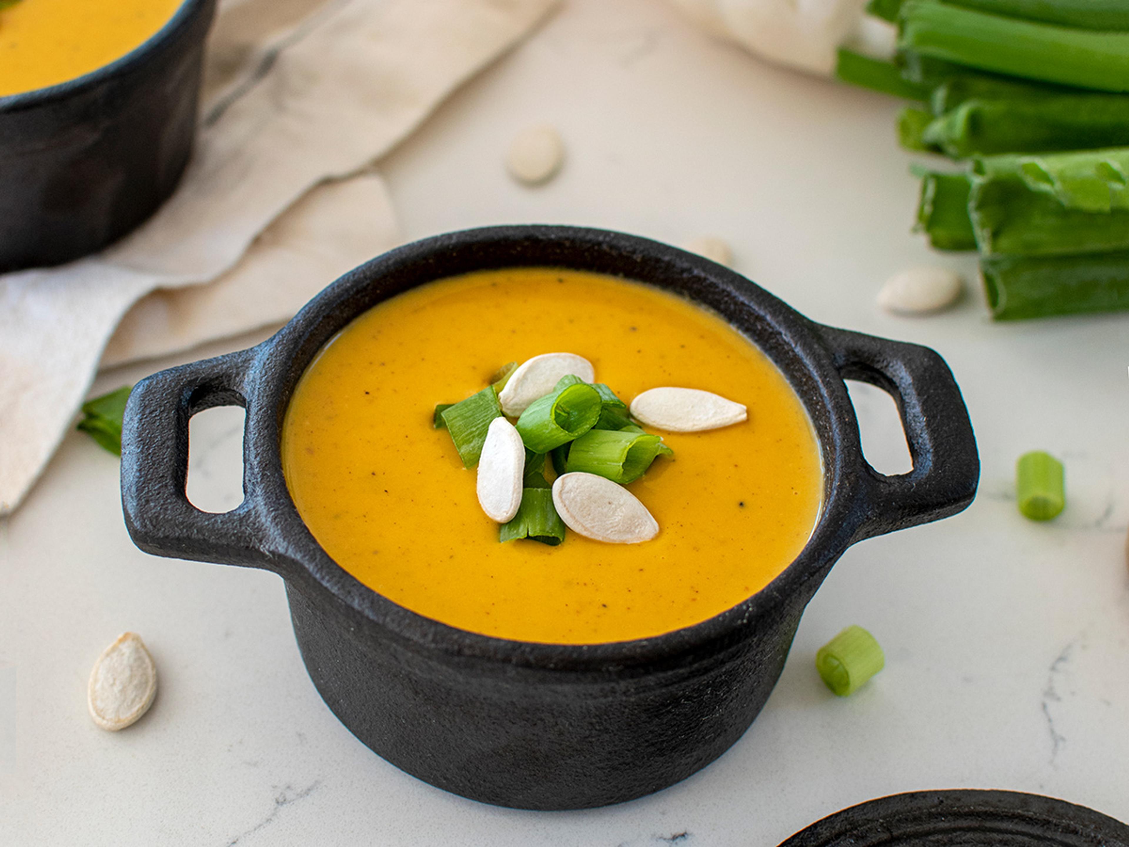 A bowl of pumpkin soup topped with green onions and white pumpkin seeds. 