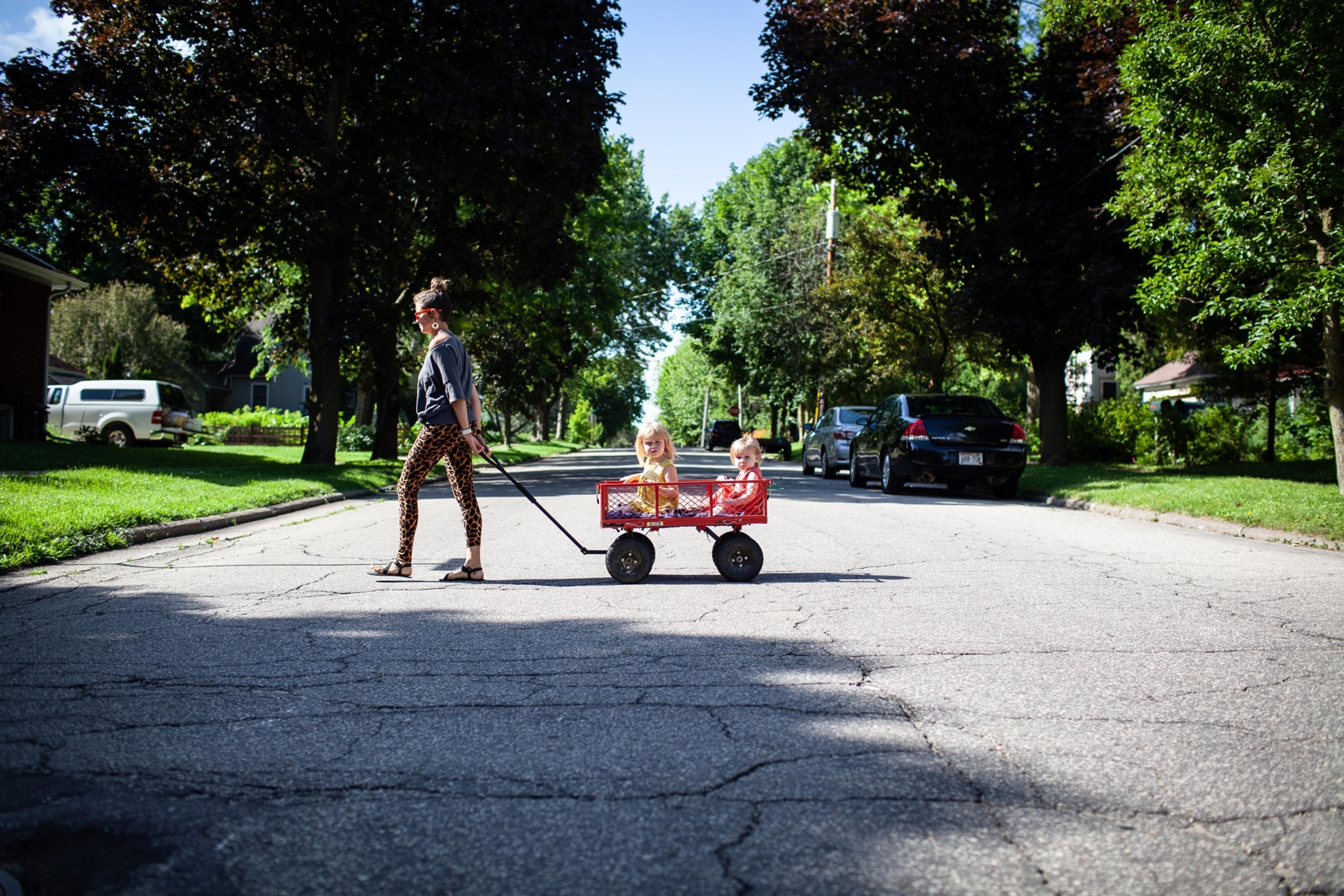 A woman pulls two children in a wagon across a small-town street.