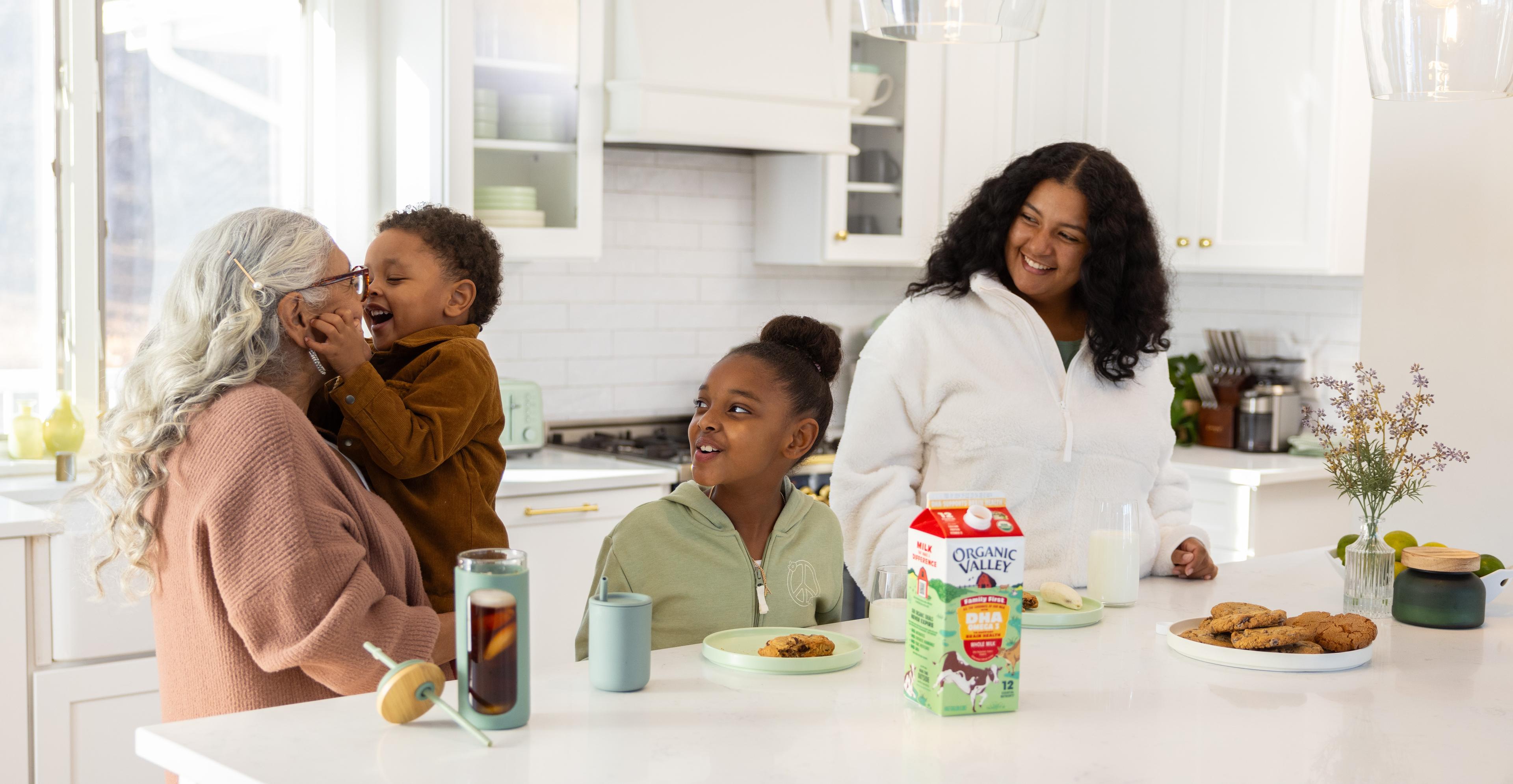 A family stands around a kitchen island with cookies and milk.