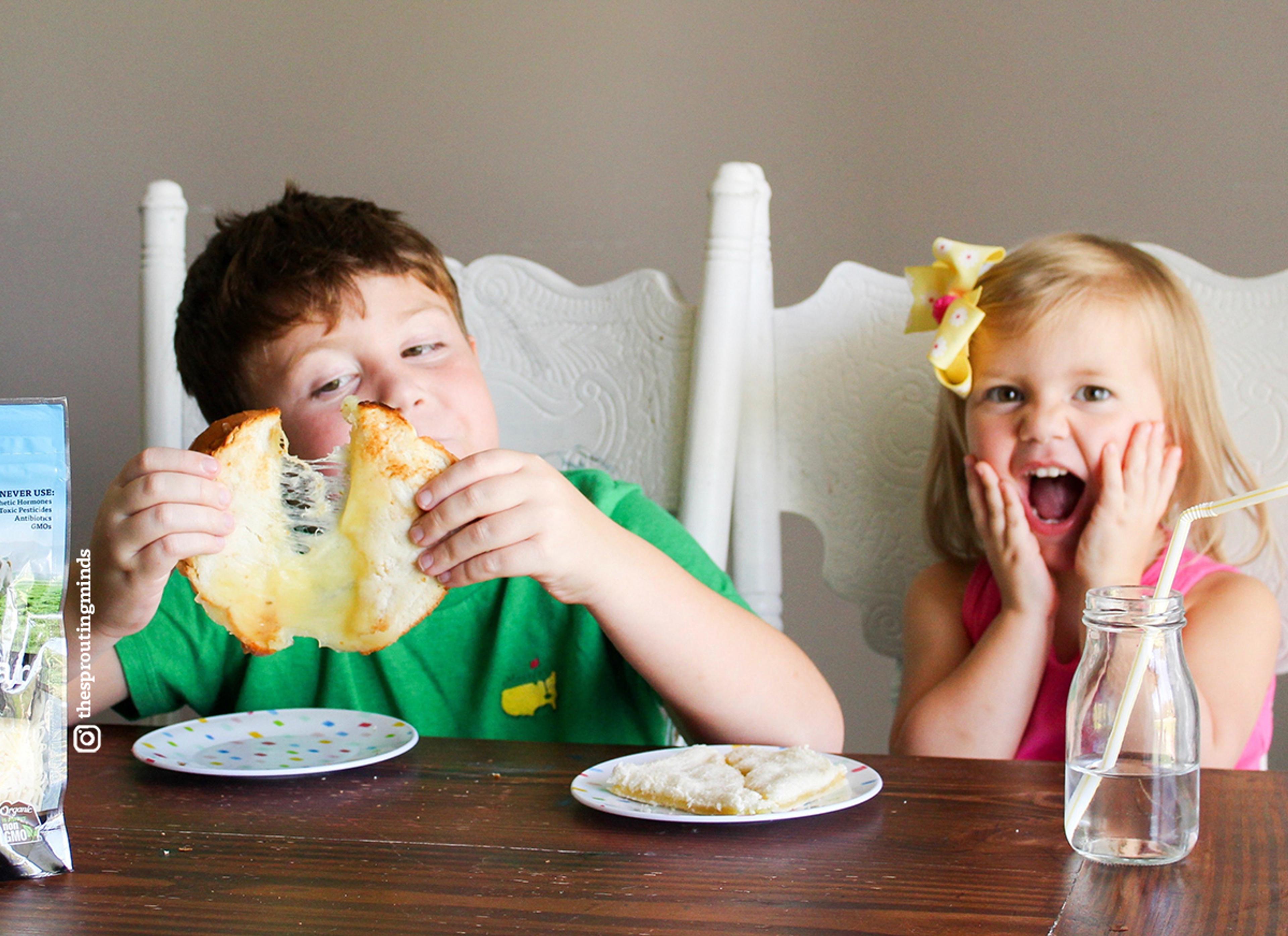 Kids sit at the table enjoying an organic grilled cheese sandwich with excited facial expressions.