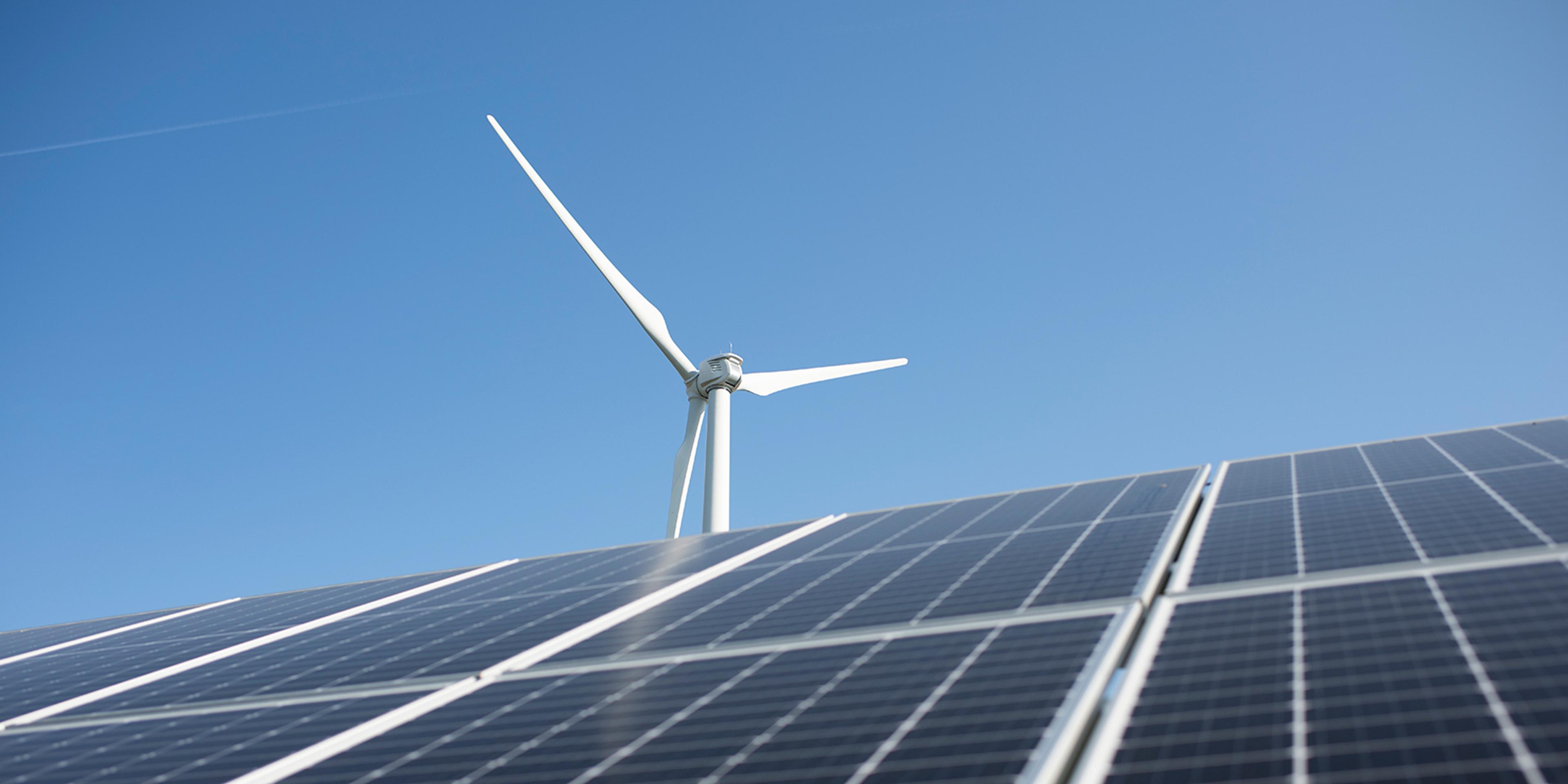 Solar panels and a wind turbine with a blue sky in the background.