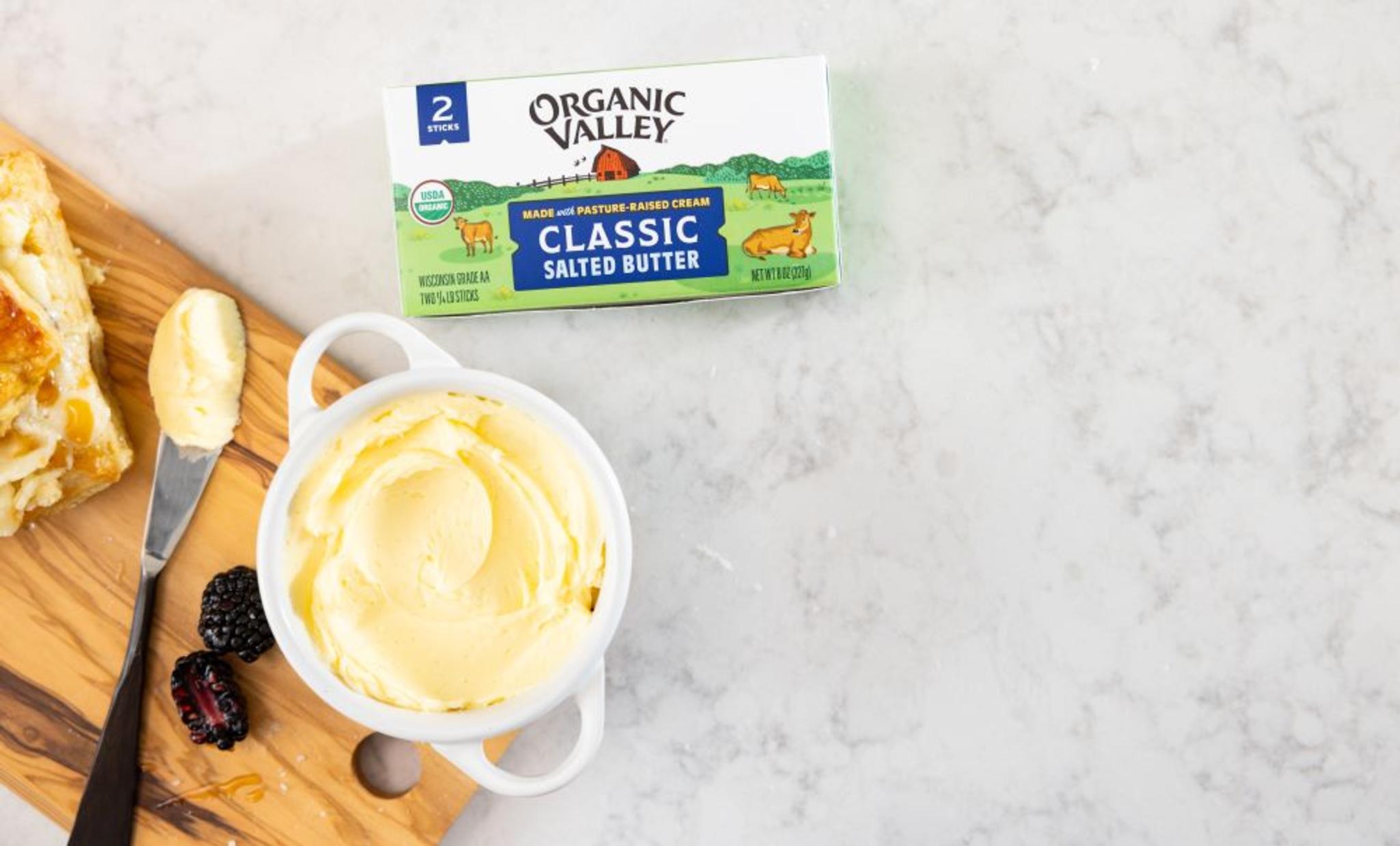 Butter in a cup with a knife and 2-pack stick of organic butter.