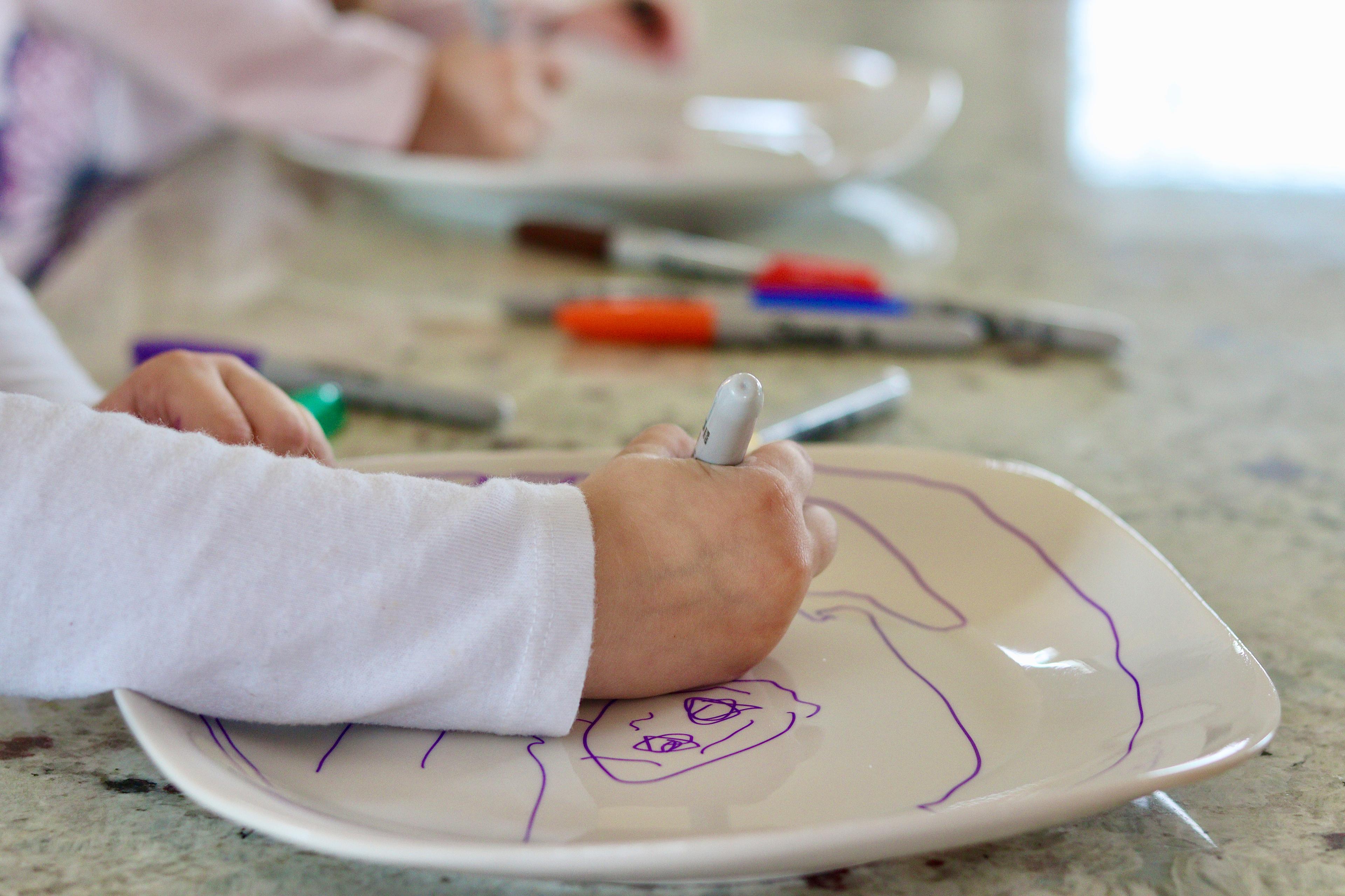 A girl colors a plate with a marker.