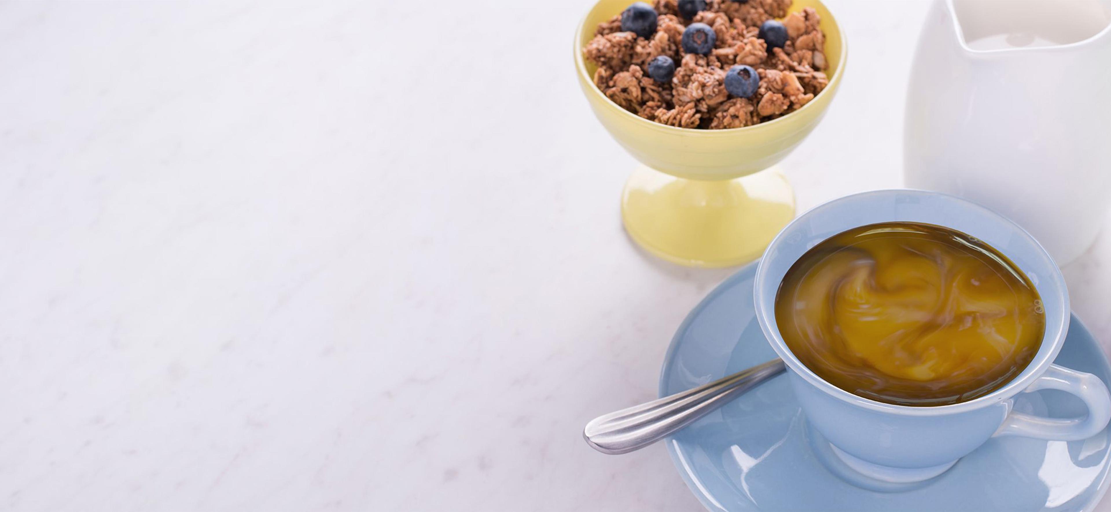 A cup of coffee with creamer in it next to a bowl of granola. 