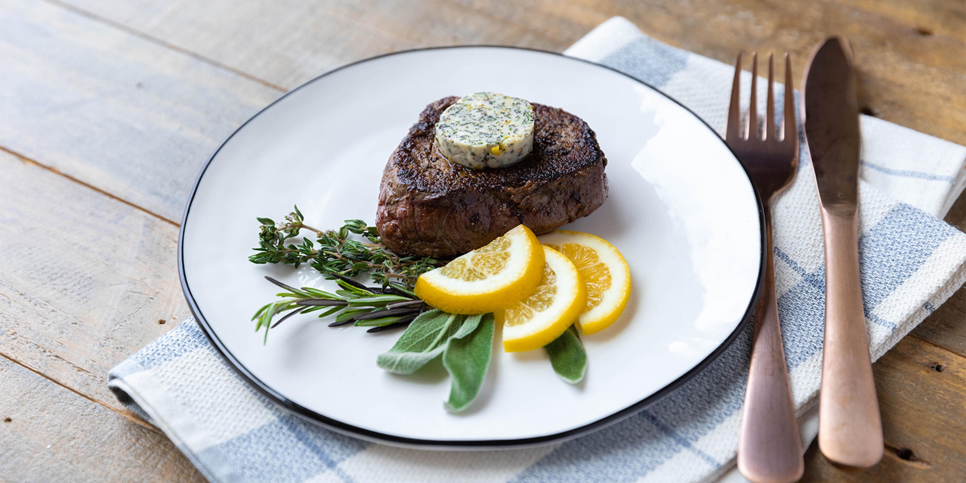 Herb Butter With Lemon Compound Butter on a steak garnished with fresh herbs.