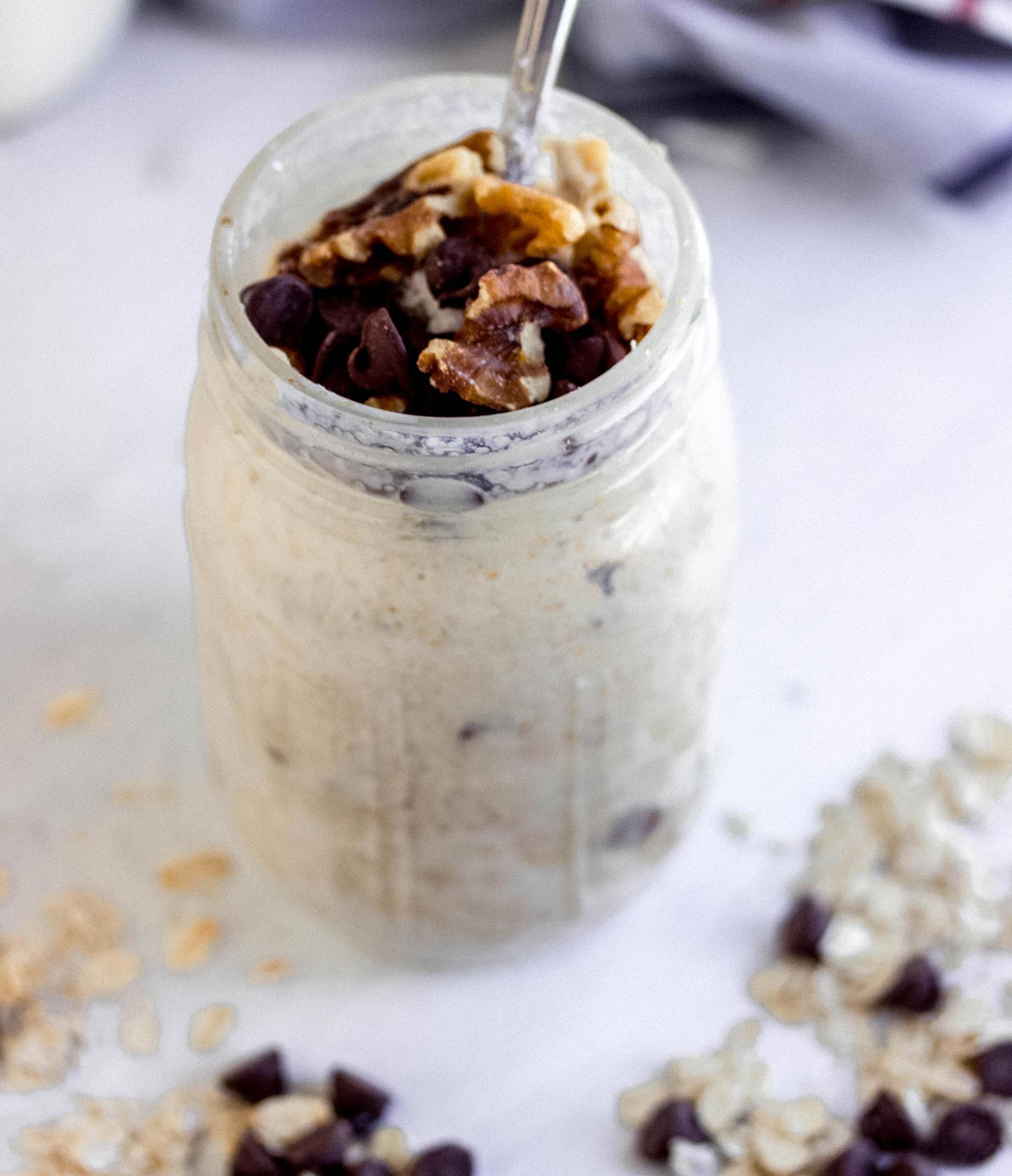 A Mason jar of chocolate chip cookie dough overnight oats topped with walnuts and with oats and chocolate chips scattered artfully around it.