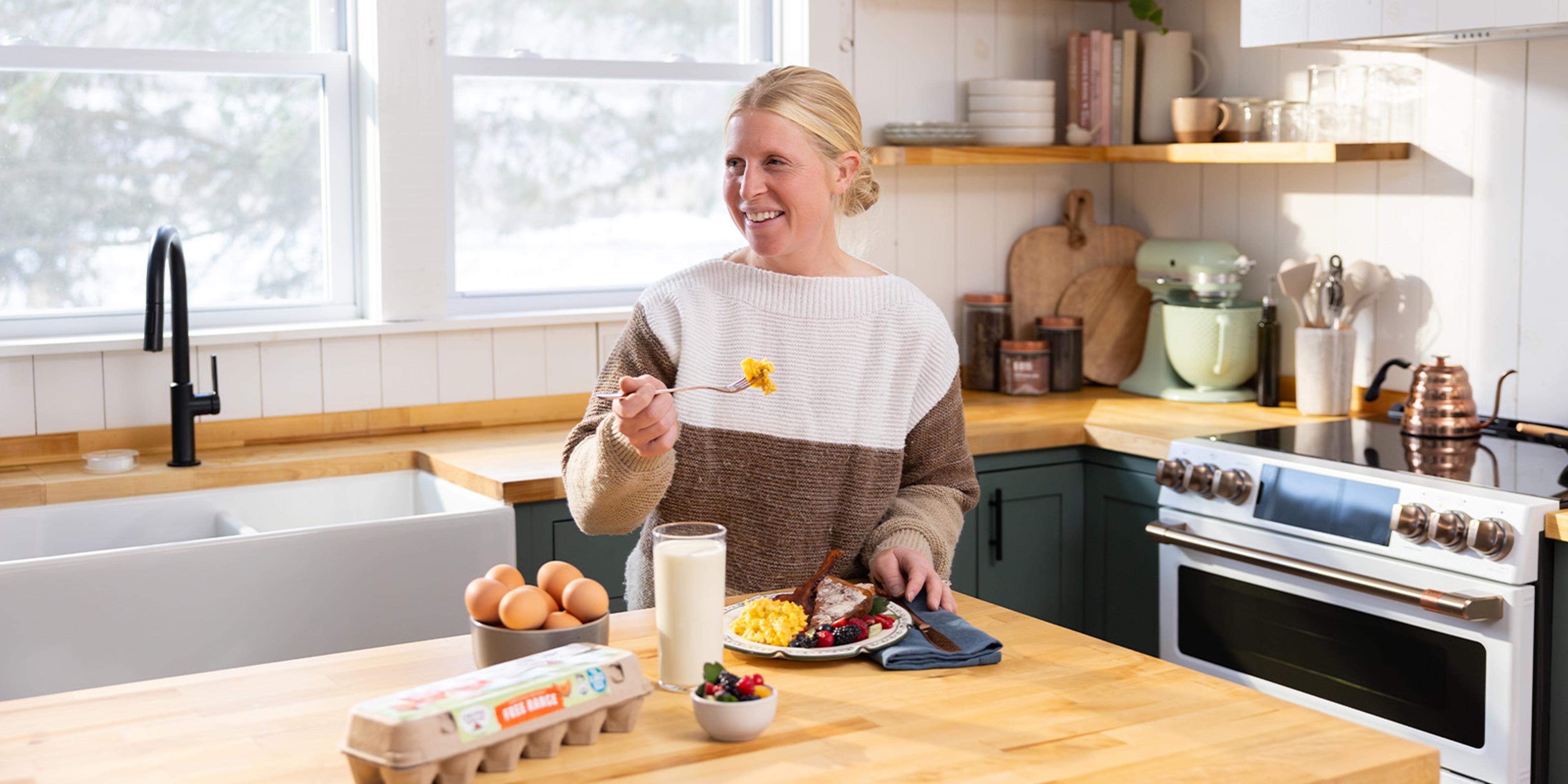 A woman eats organic breakfast foods in a kitchen.