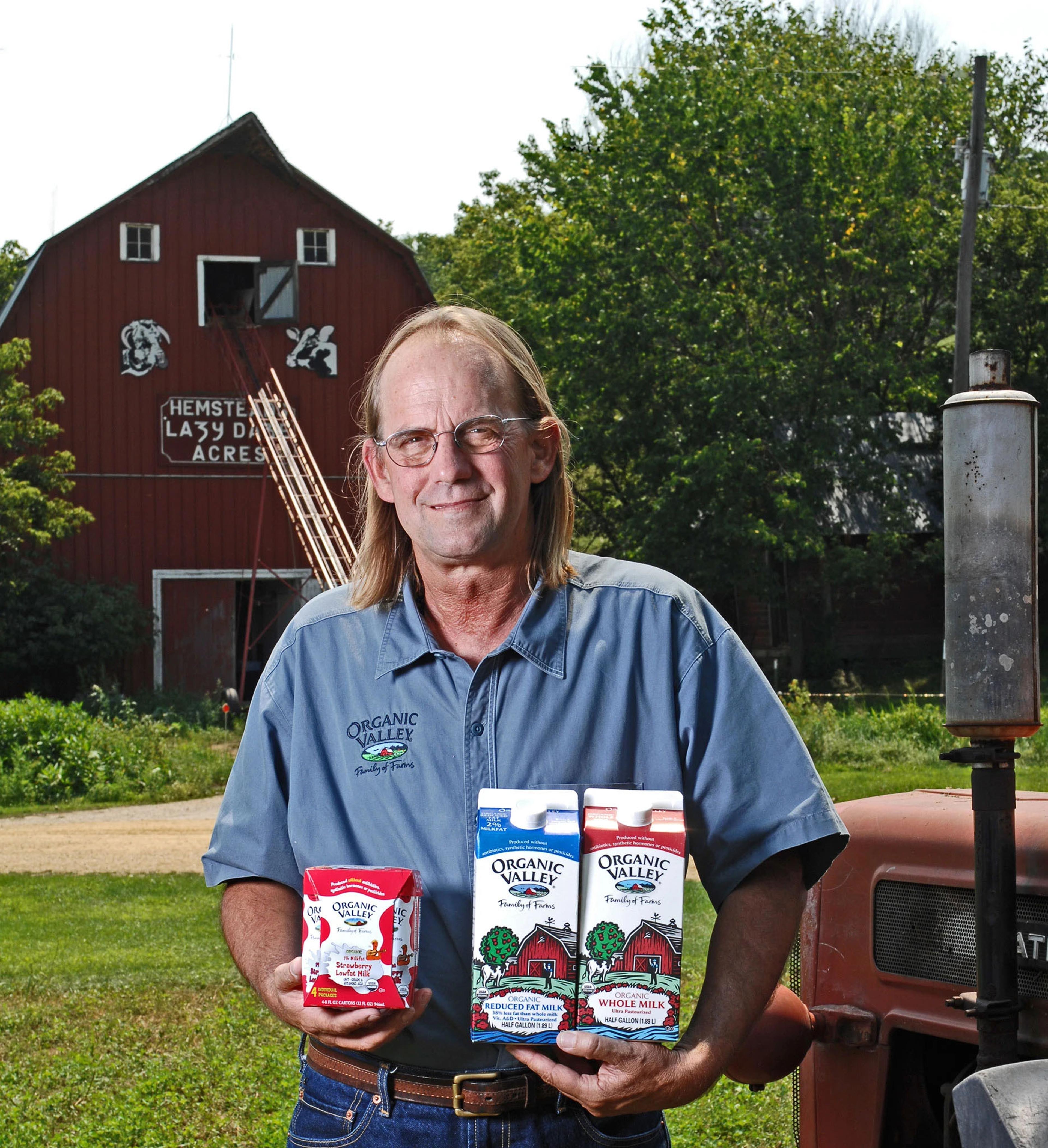 Organic Valley’s founding CEO, George Siemon, holds cartons of Organic Valley milk while standing in front of a barn.