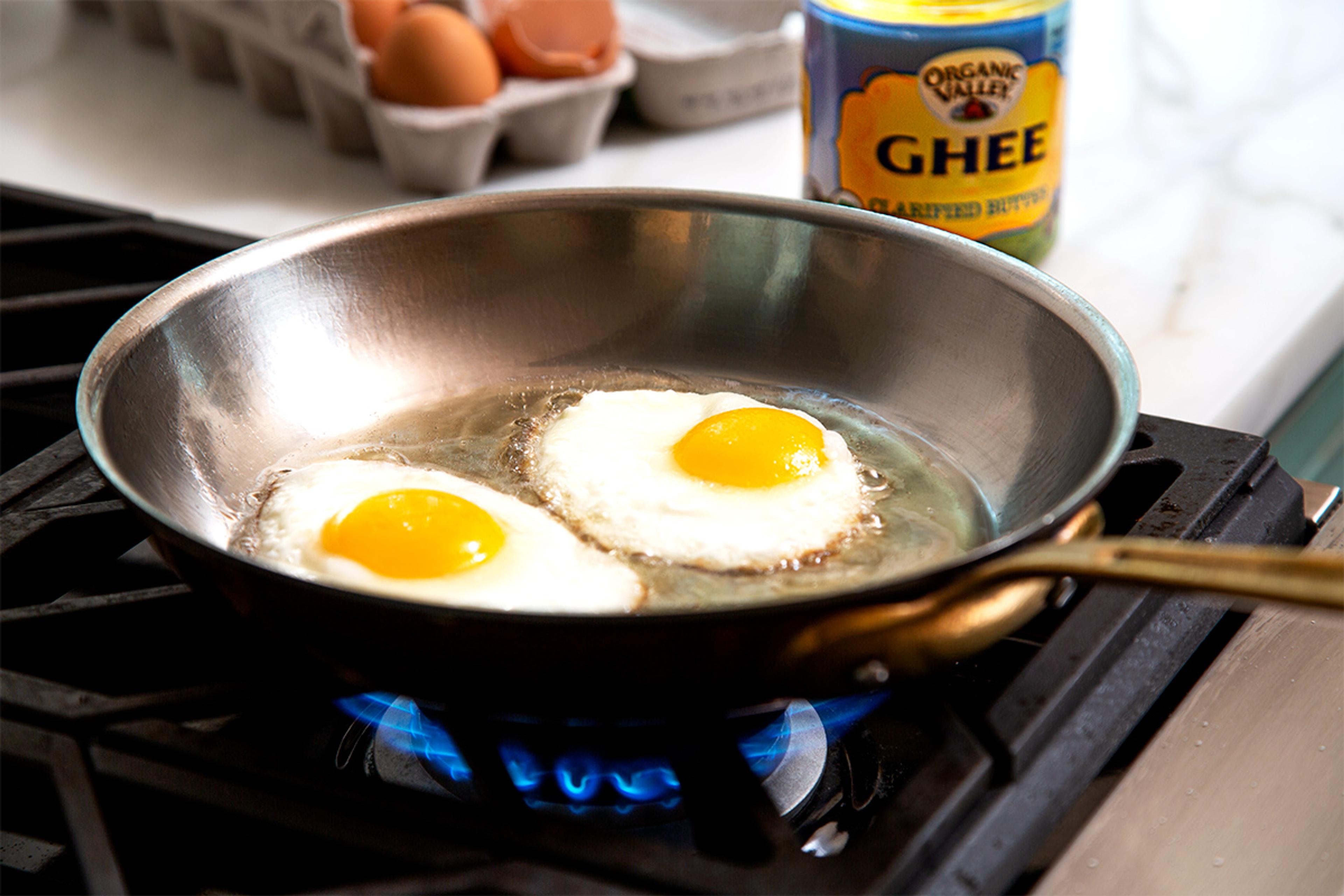 Two fried eggs sizzle in a pan with Organic Valley ghee.