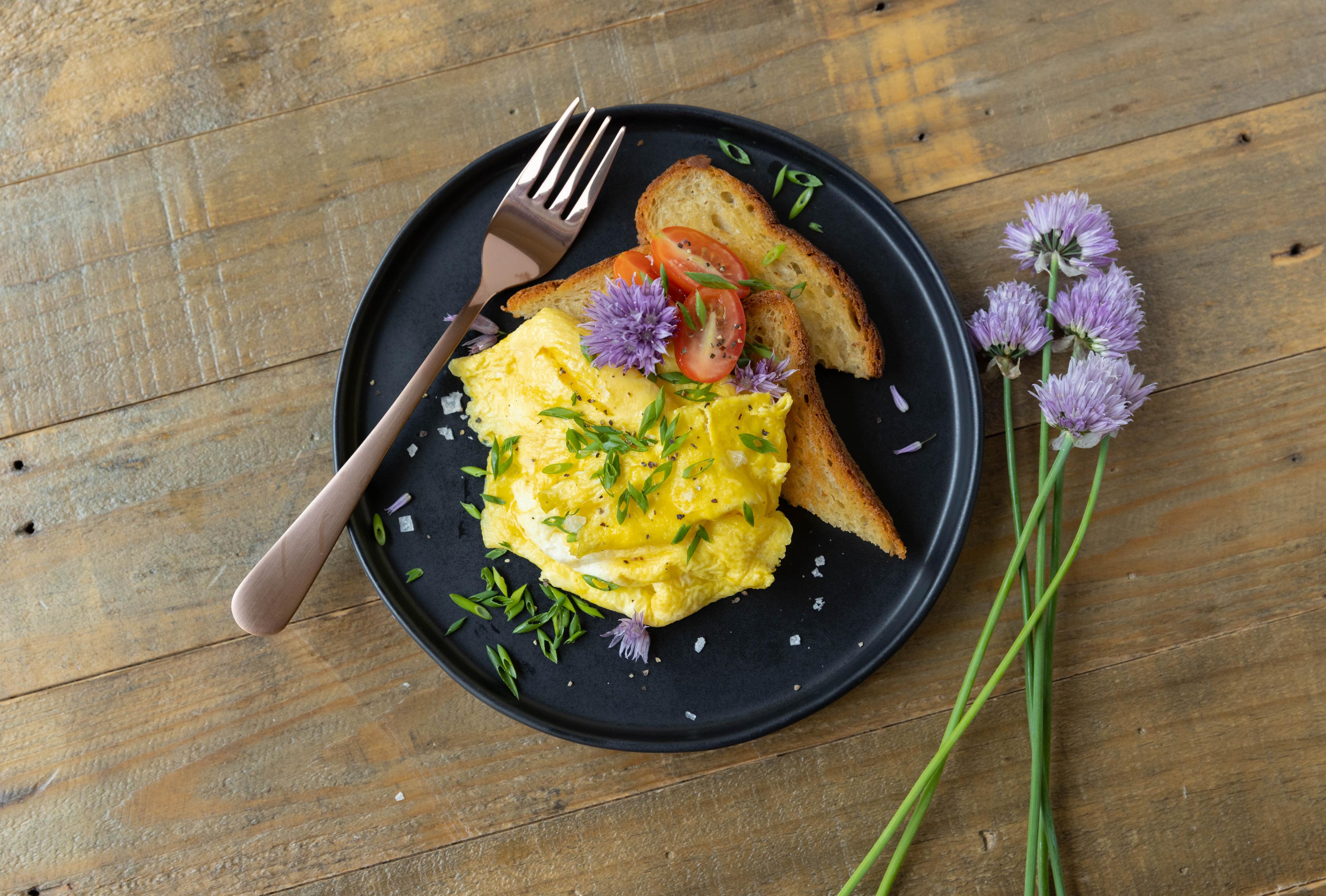 Chives on scrambled eggs with toast and tomatoes.