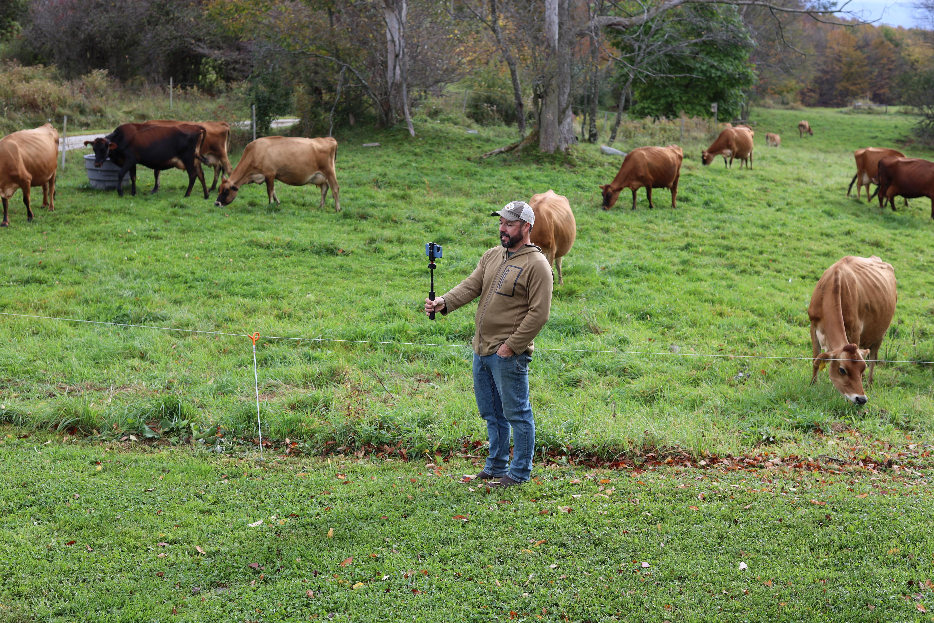 Vermont farmer Tyler Webb holds a camera as organic dairy cows graze in the background.