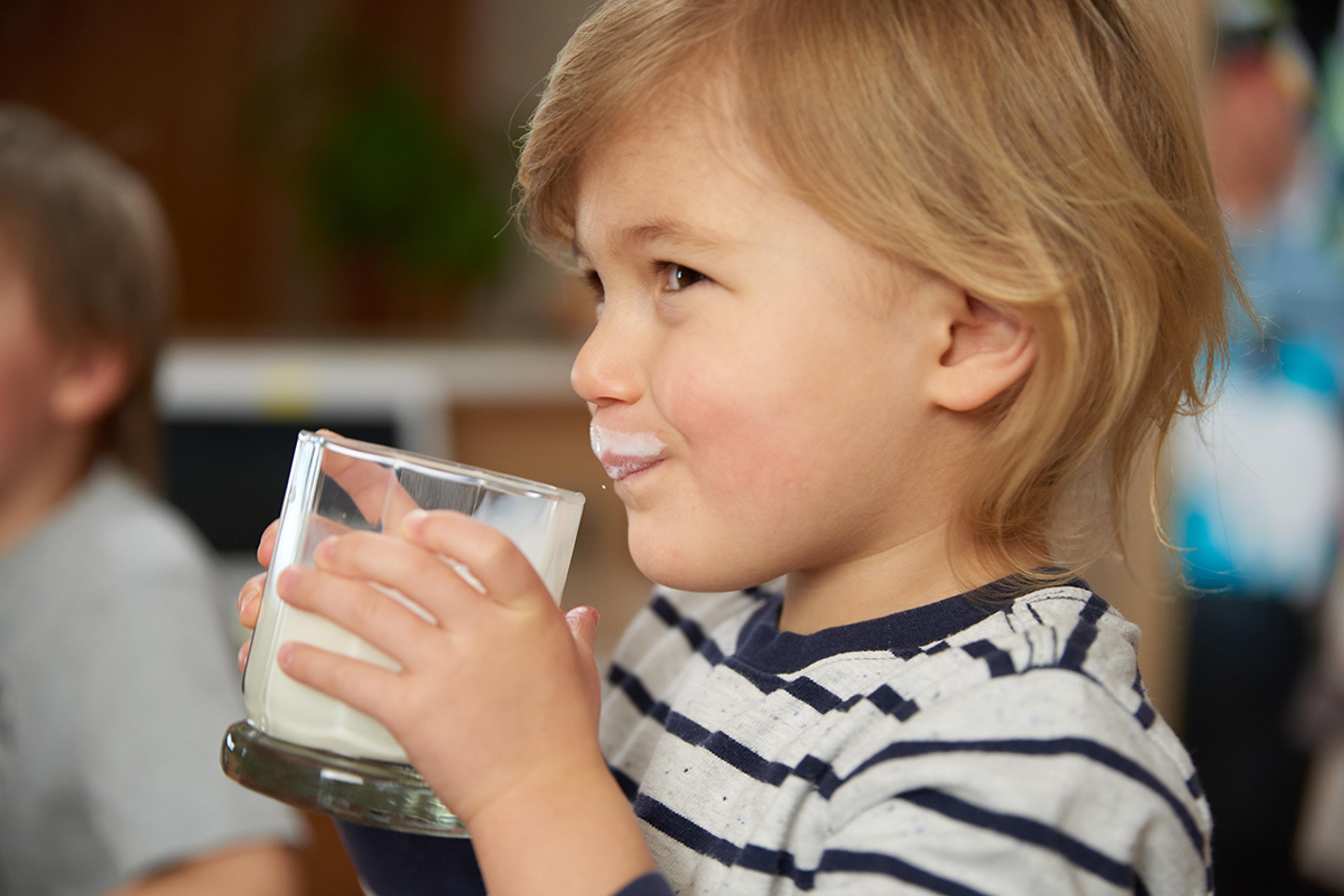Young boy with a milk mustache drinks a glass of organic milk.