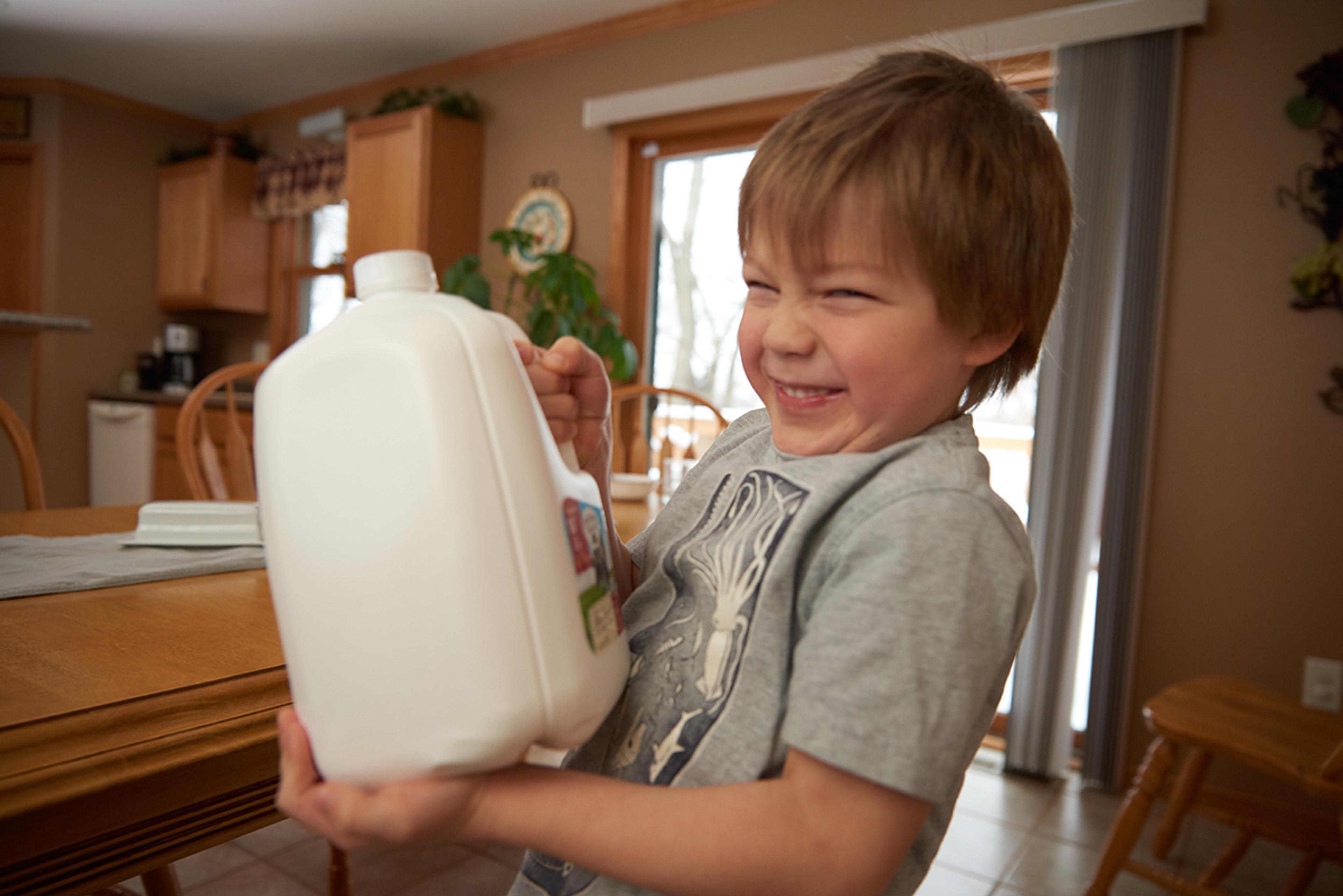 Young boy holds a gallon of Organic Valley milk and smiles to the camera.