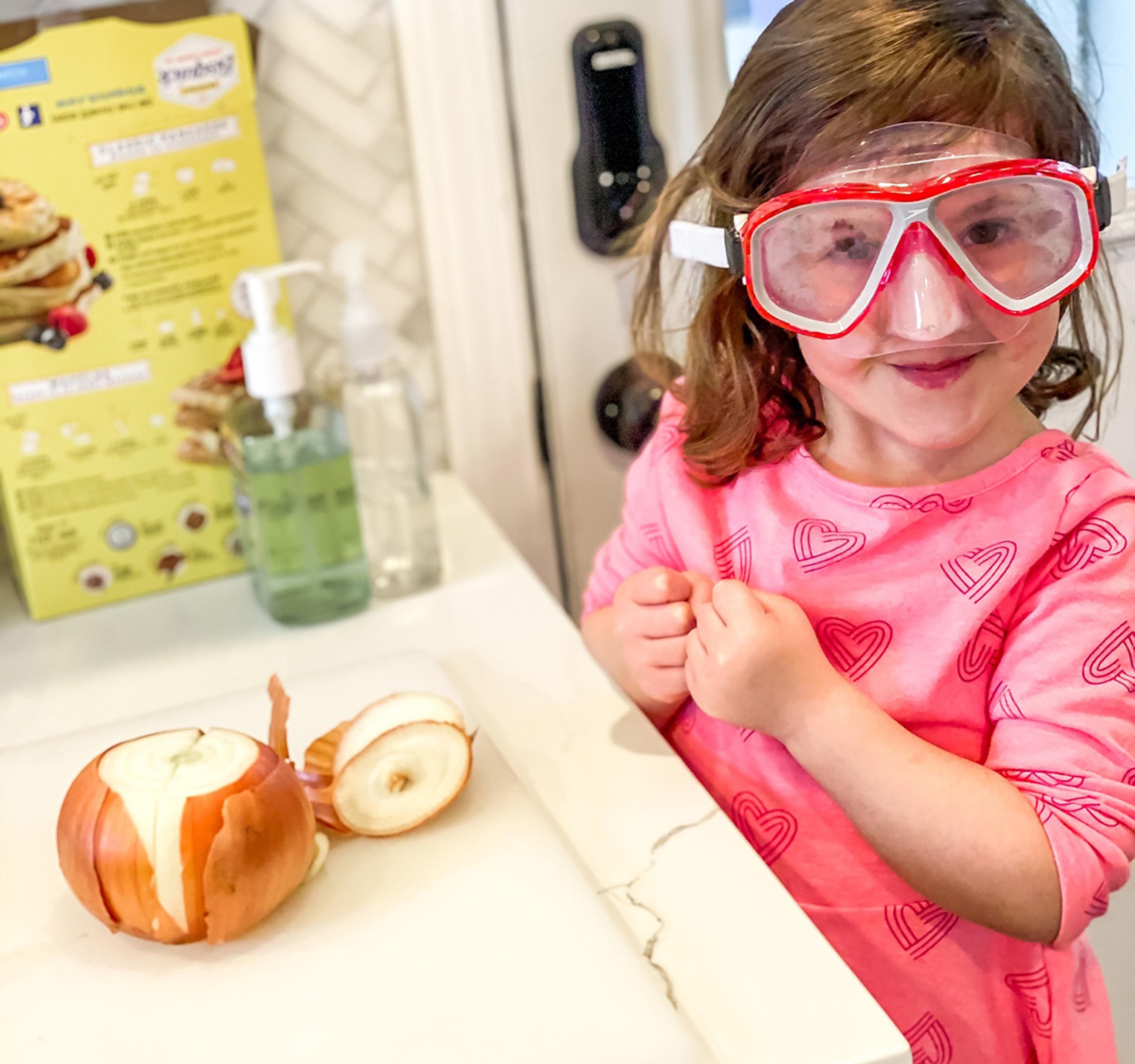 Young girl in goggles cuts up an onion in the kitchen.