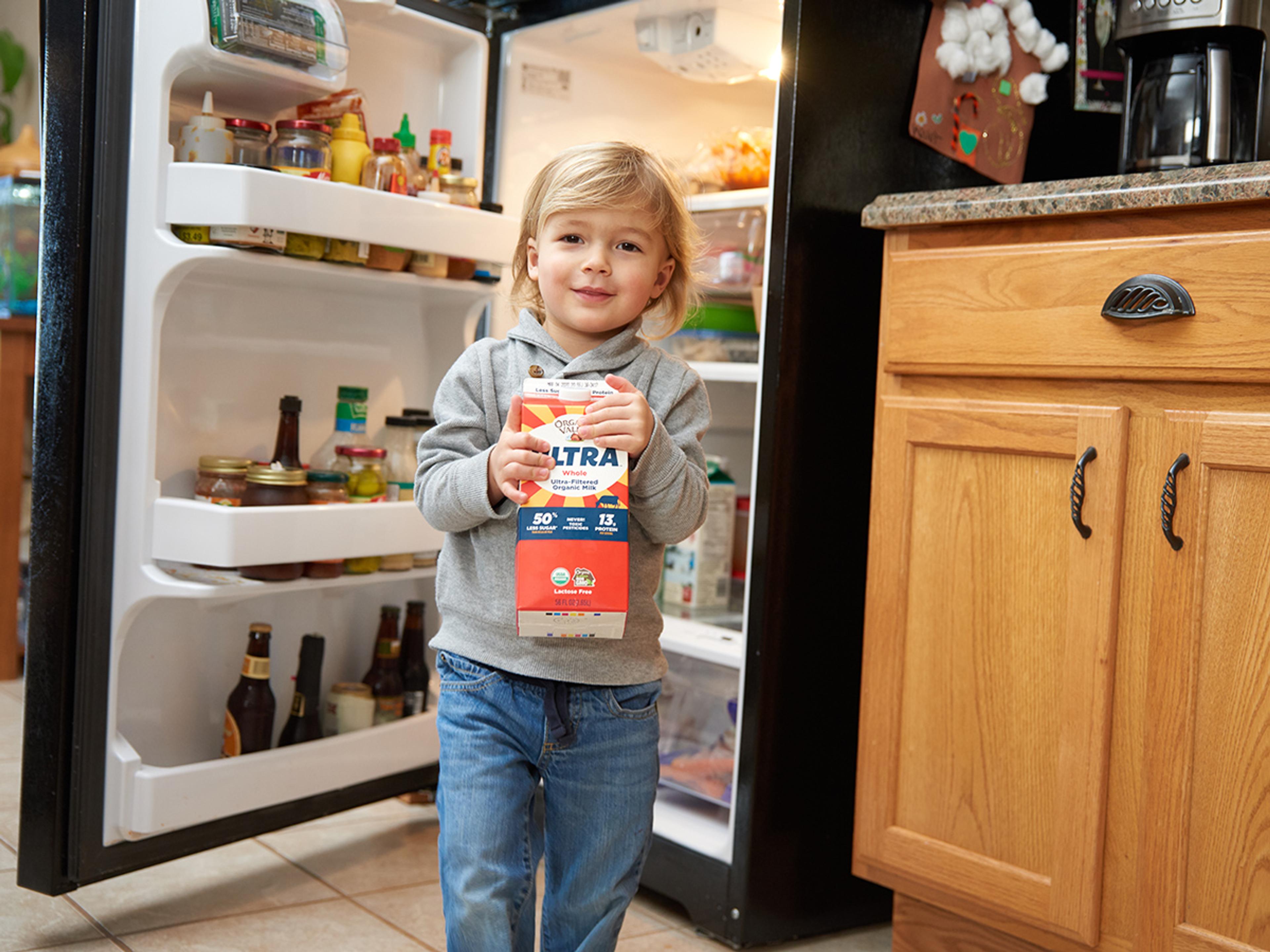 Young boy happily carries a carton of milk in the kitchen.