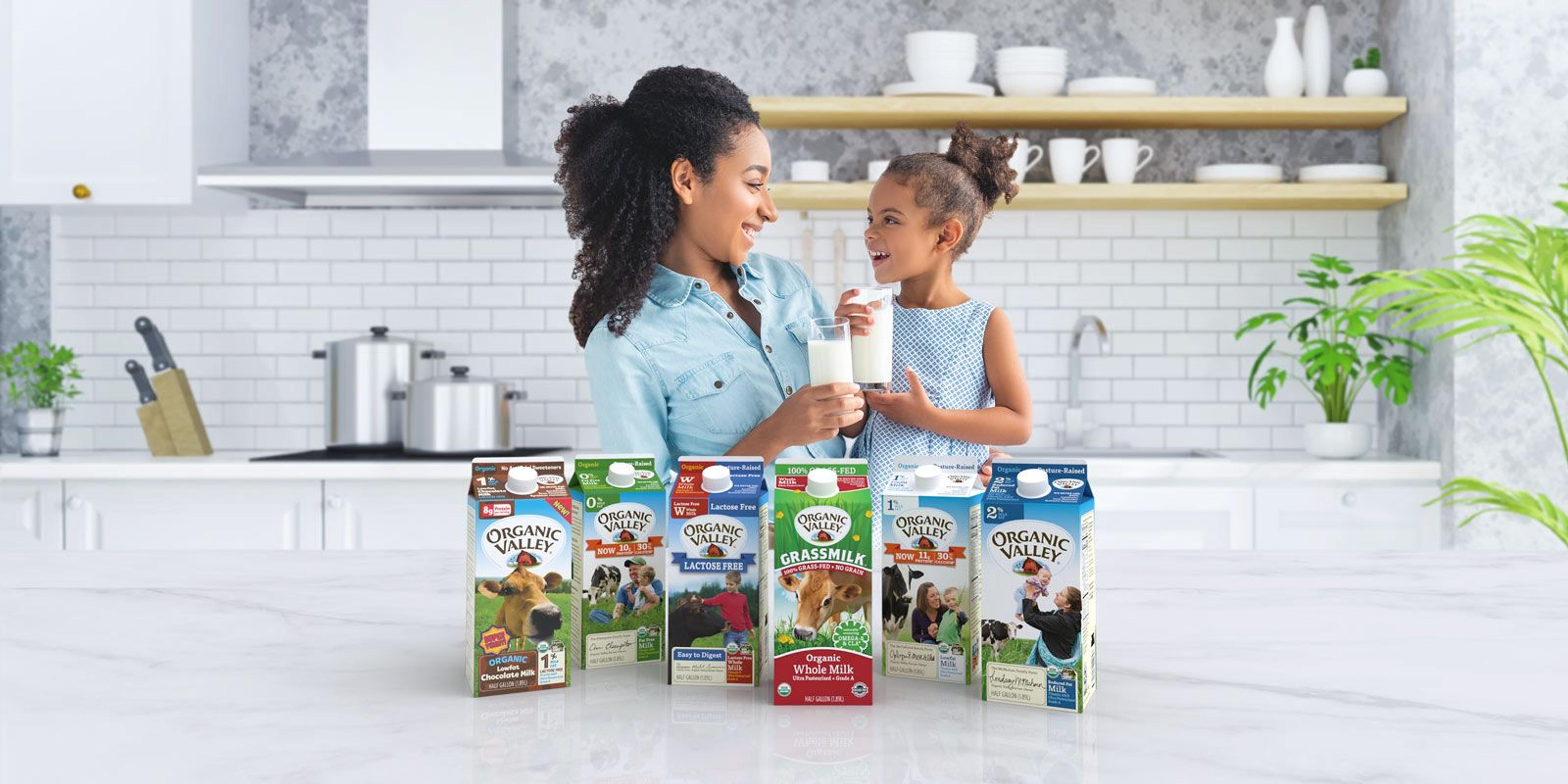 A mother and daughter hold glasses of milk while standing against a wall displaying Organic Valley milk cartons.