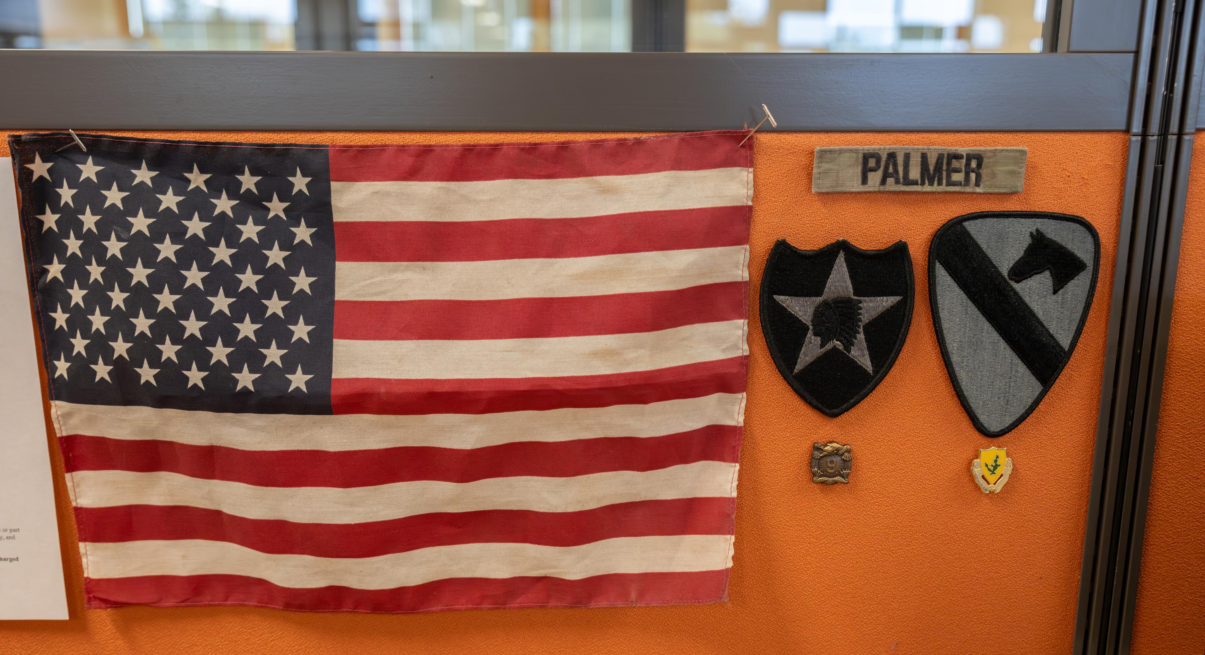 An American flag and Army patches hang by Eric Palmer's desk. Photos of his children are shown on his computer.