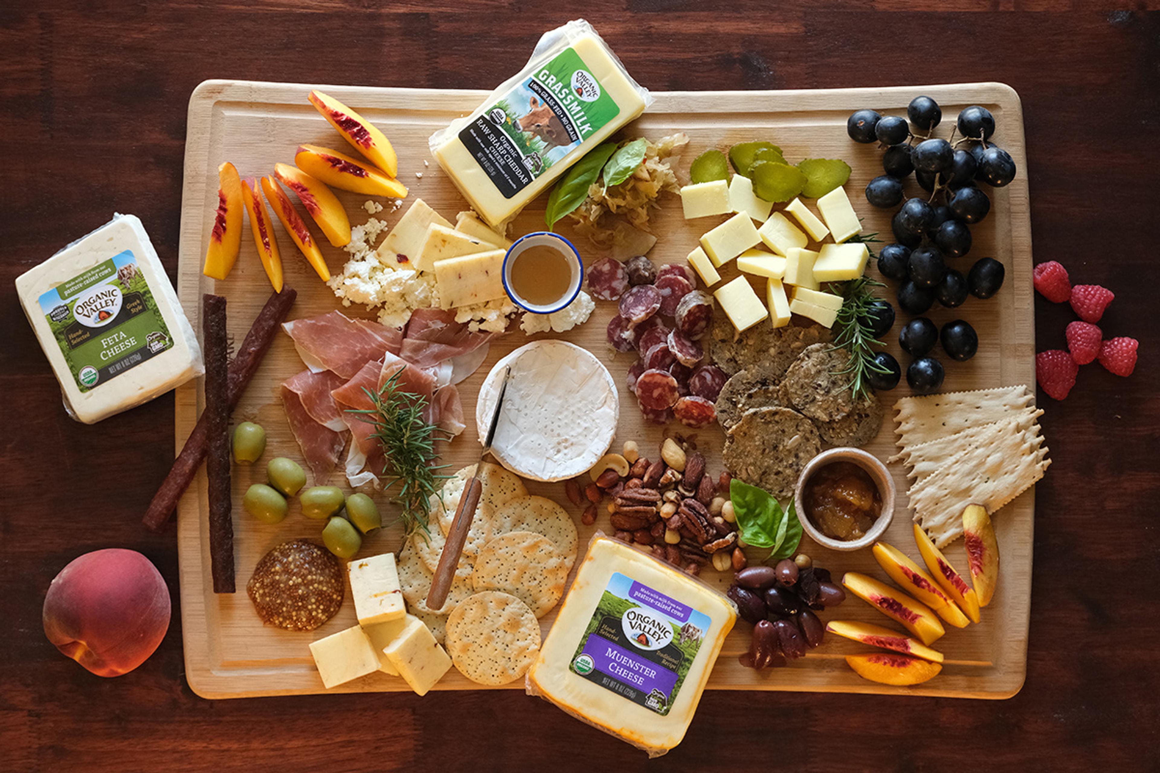 An overhead view of an artful cheese board containing cheese, means, crackers, tips, fruits and nuts.
