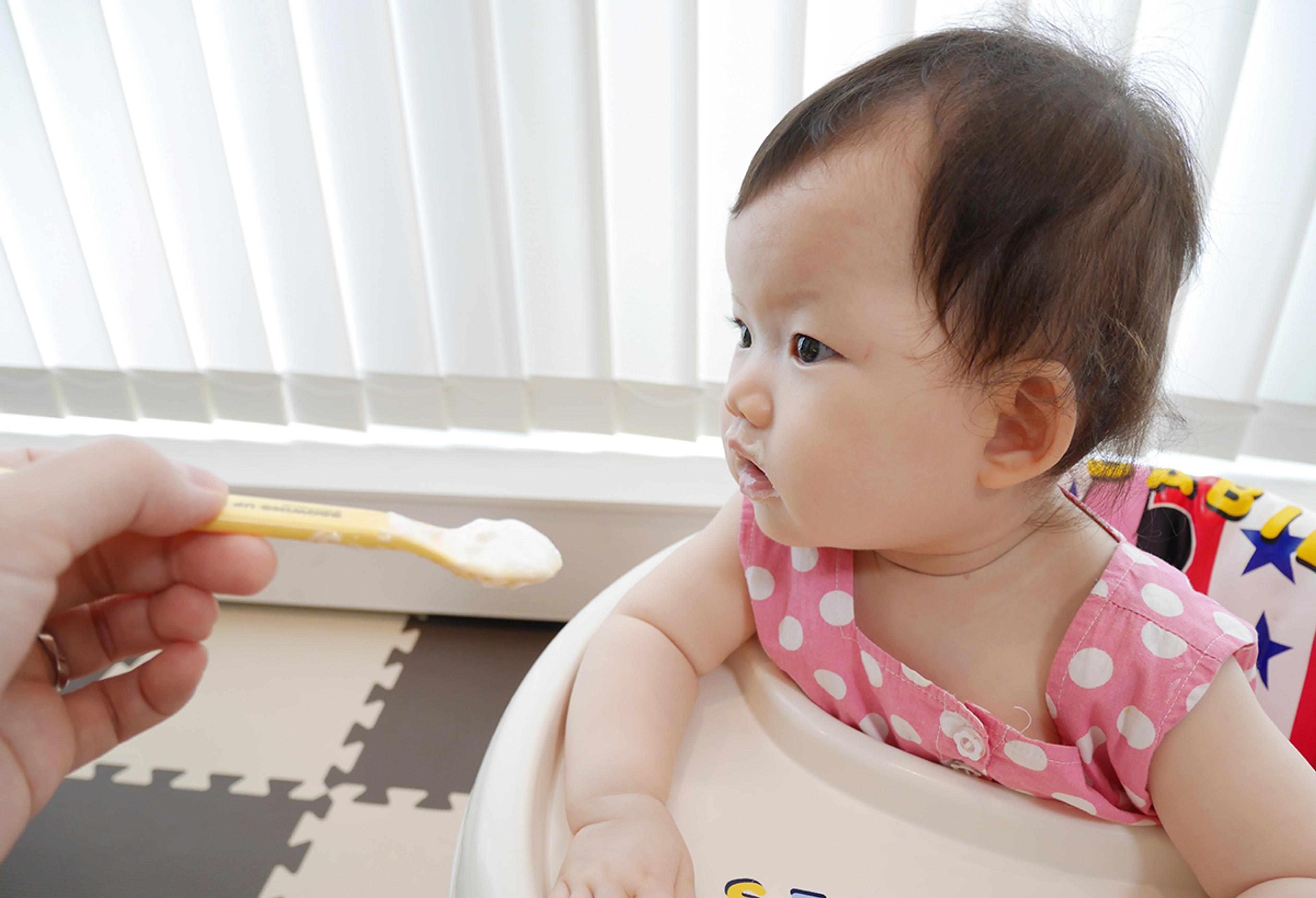 Asian baby gets spoon fed yogurt in her high chair.