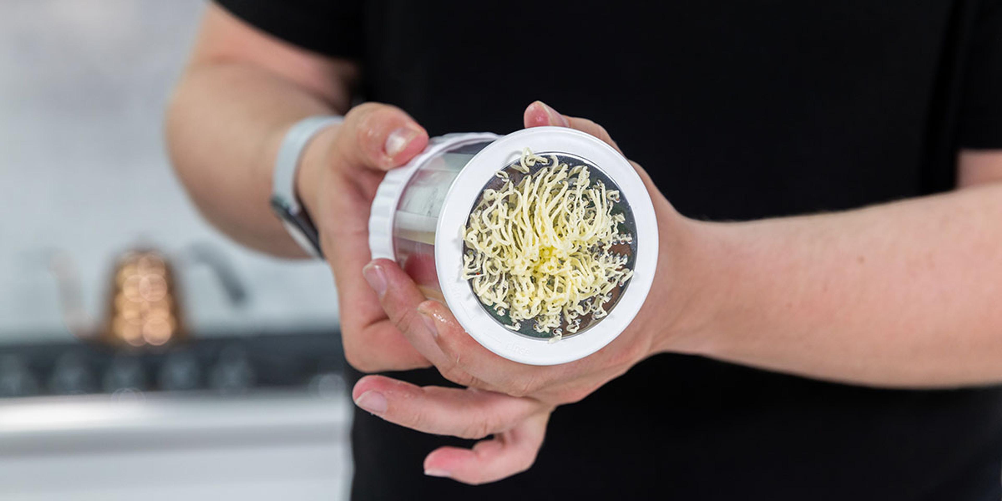 A man turns the knob on a butter mill and squiggly noodles of butter comes out.