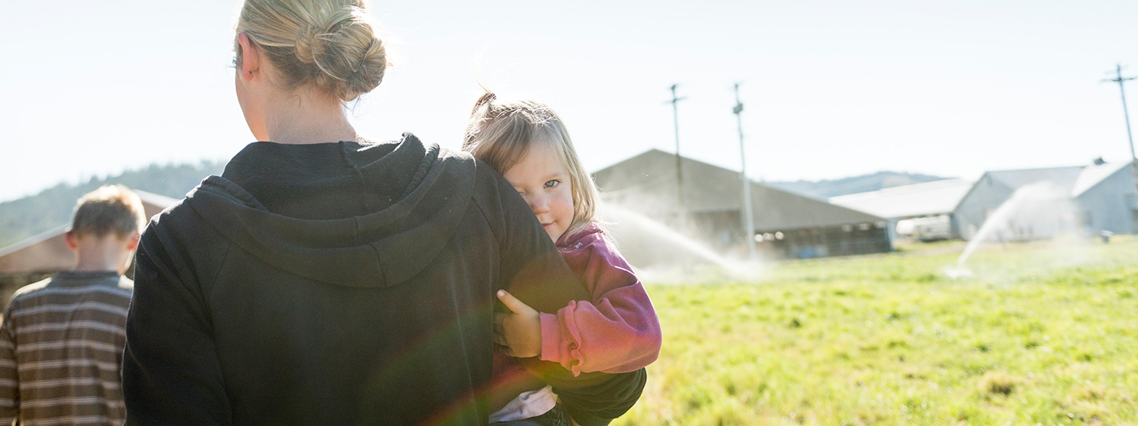 Young girl looking over her mother's shoulder as she's carried across the farm.