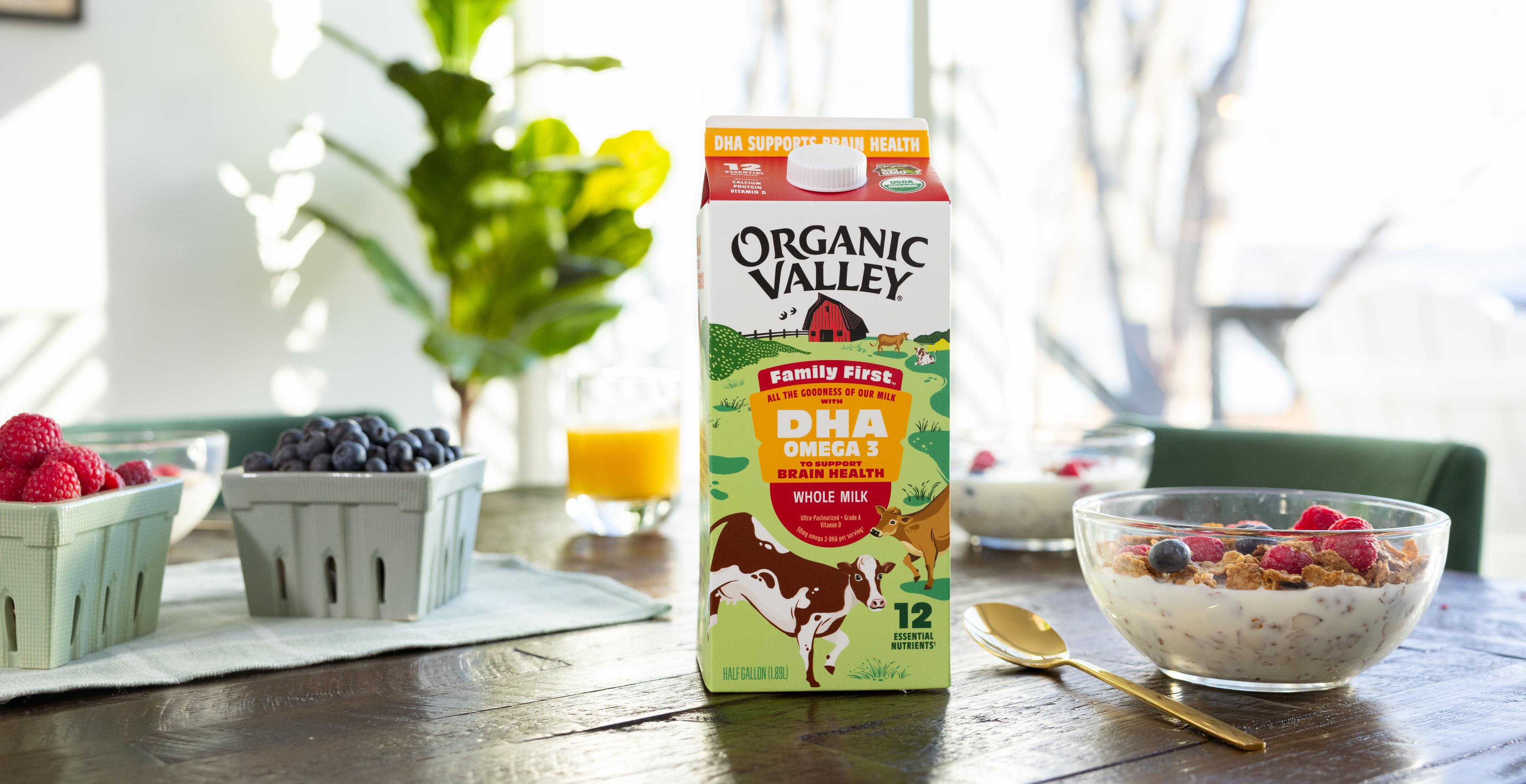 A carton of organic milk on a table with berries, juice and granola.