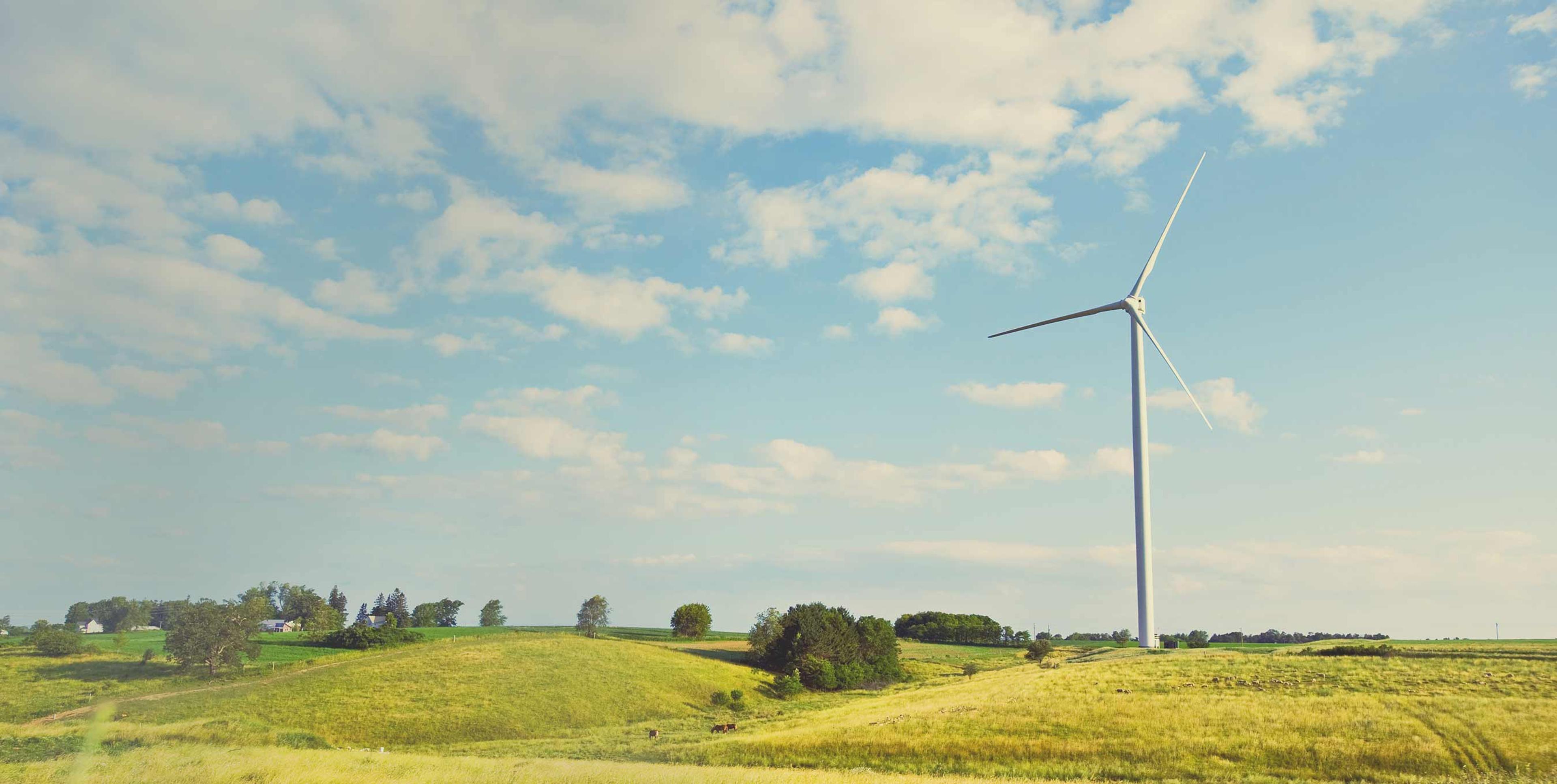 A windmill sitting on a hillside of green gras amongst a blue, cloudy sky.