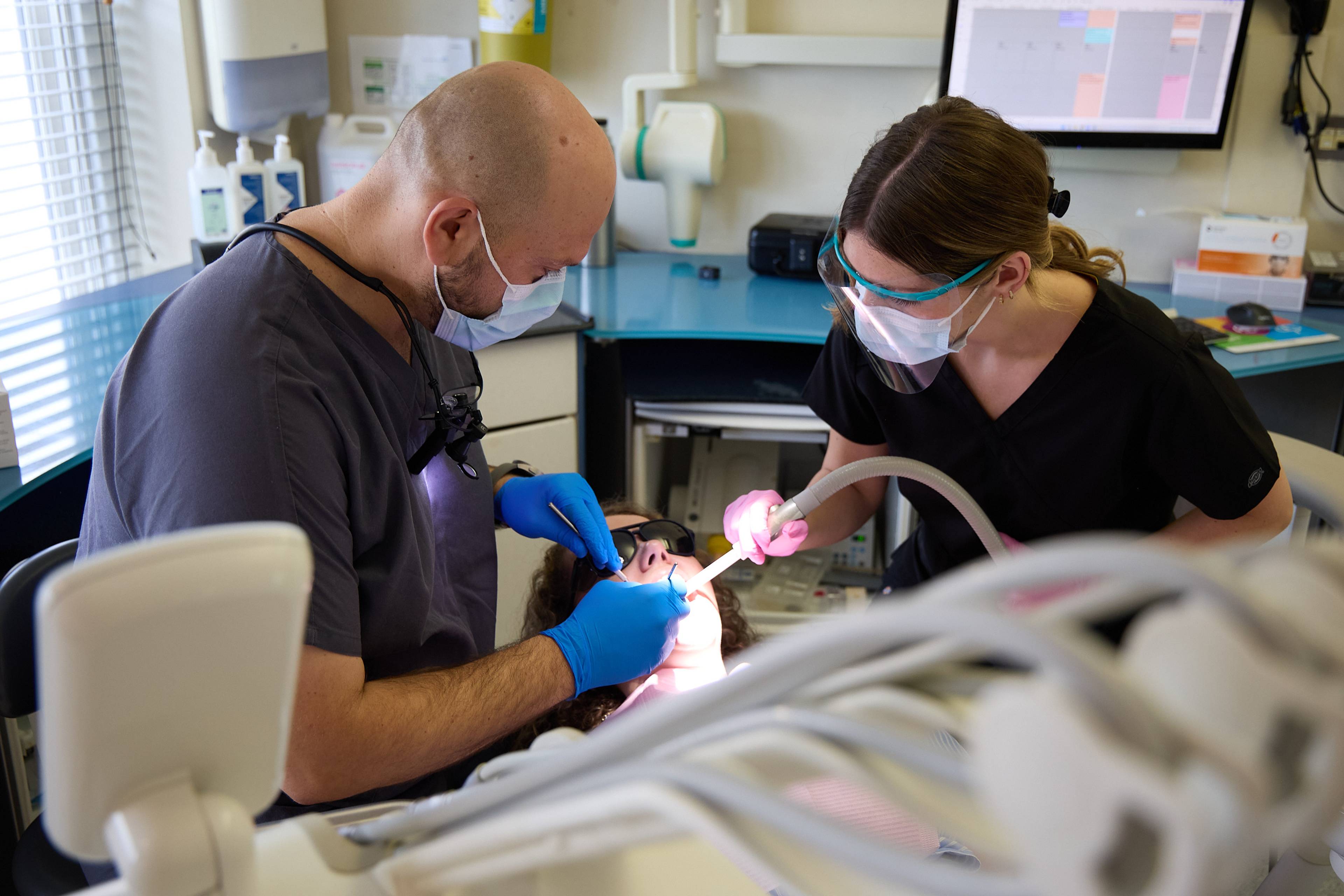 Dental team providing treatment to a patient using modern clinical instruments and suction equipment at Bath Spa Dentistry.