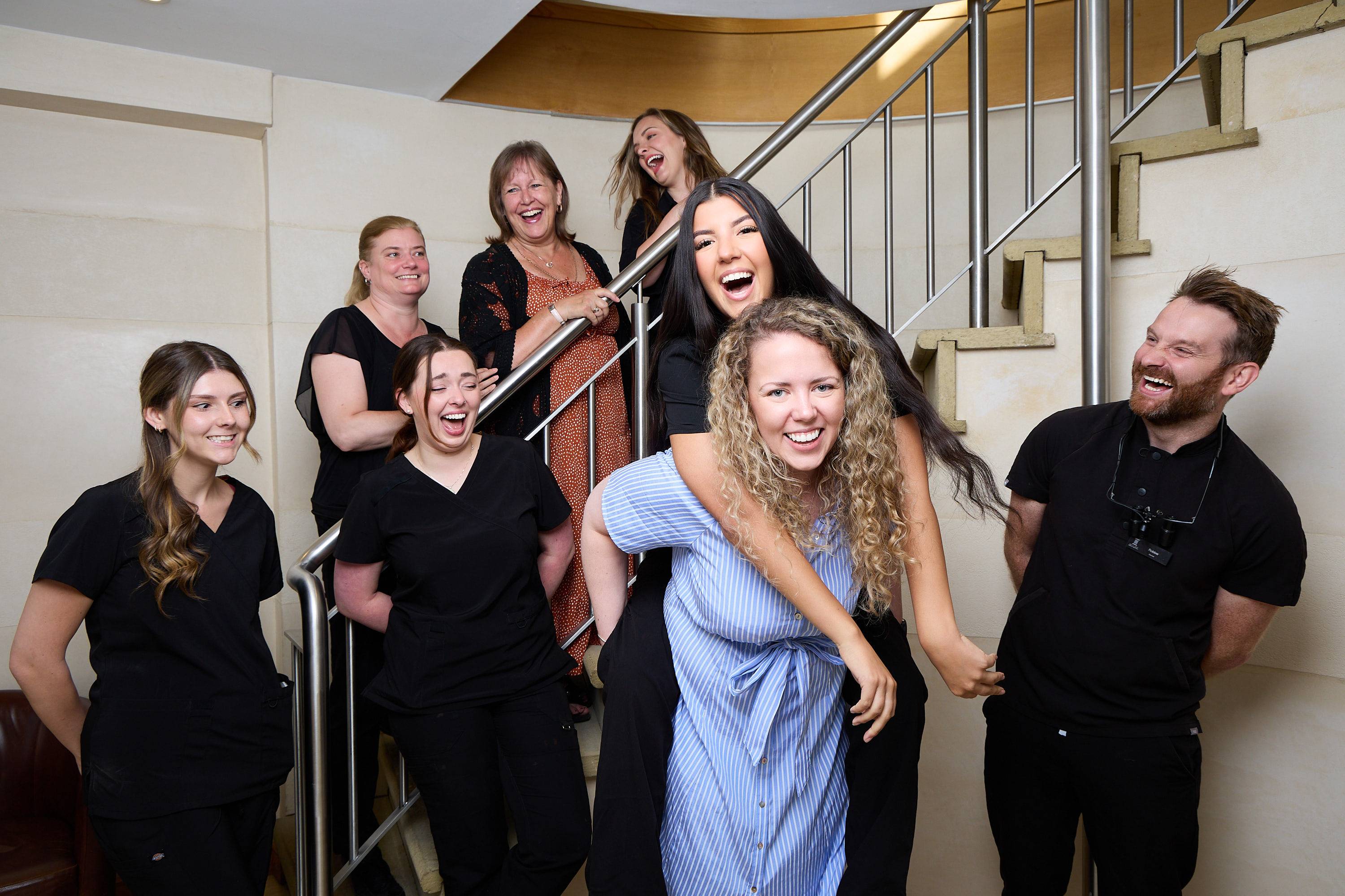 Bath Spa Dentistry team members posing for a fun and informal group photo on a staircase inside the practice.