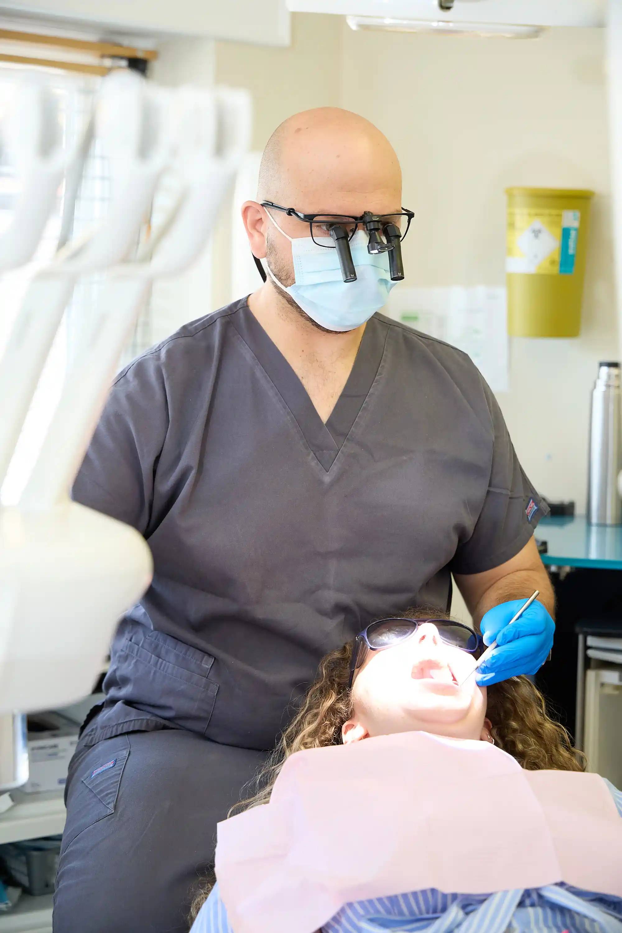 Dentist performing a routine dental examination on a patient using magnification loupes and modern clinical instruments at Bath Spa Dentistry.