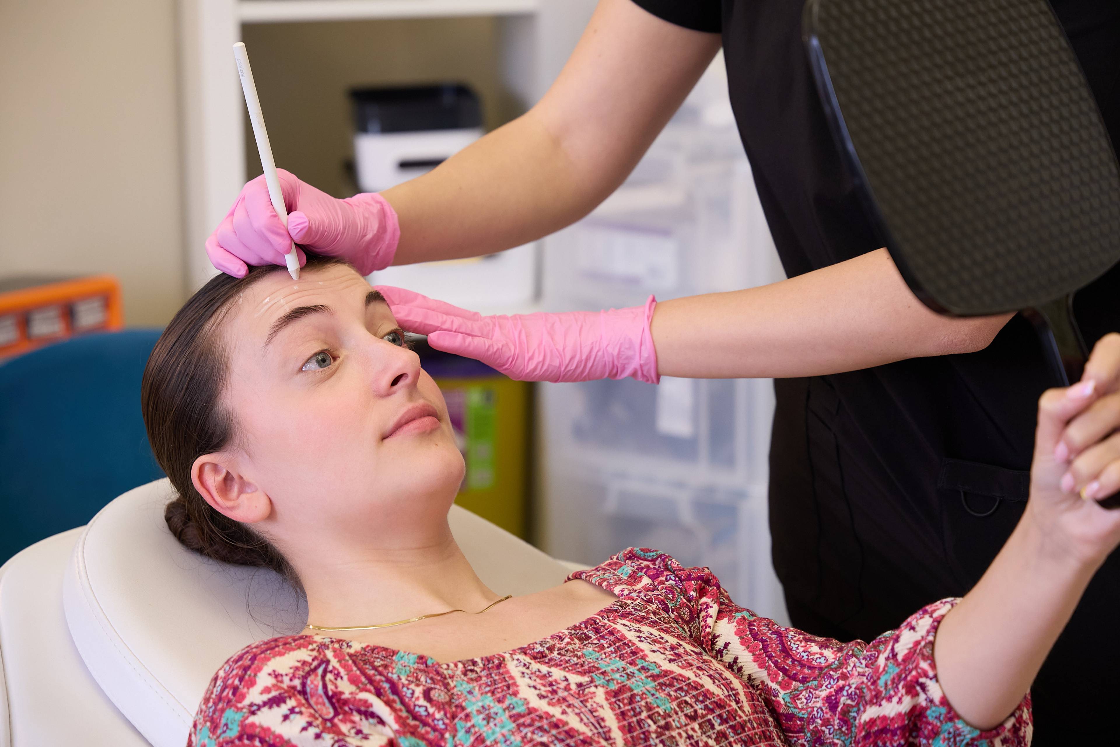 Patient holding a hand mirror during a facial aesthetics consultation while a clinician marks treatment areas at Bath Spa Dentistry.