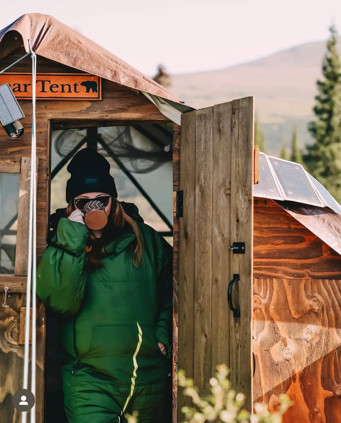 Emily sips tea from a mug within a tent in the Alaska wilderness