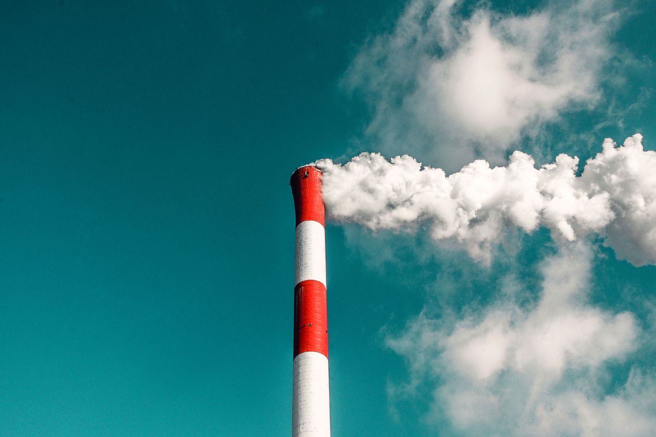 Red and white exhaust tower emitting cloud of burnt fossil fuels