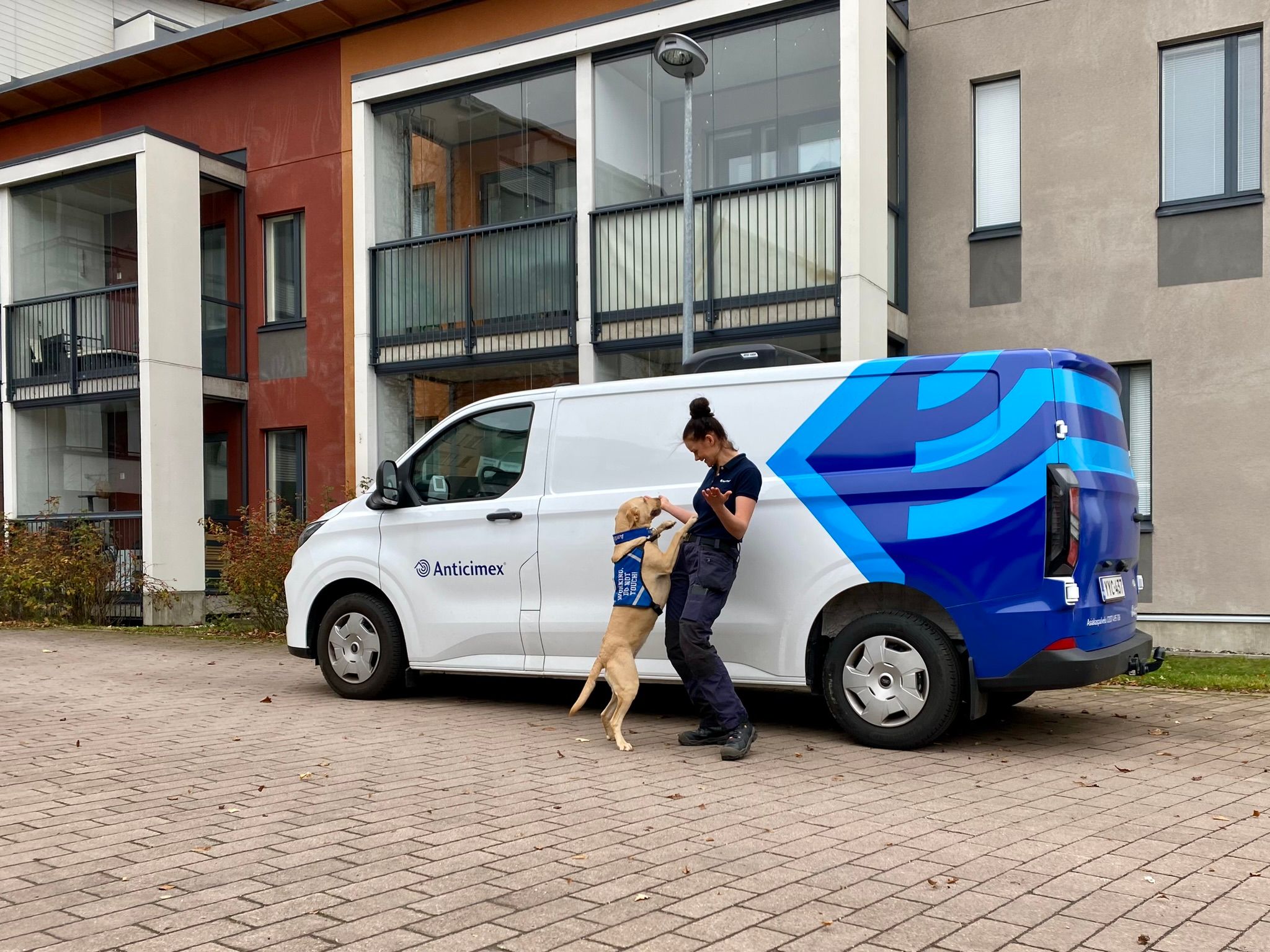 Lutikkakoira ja koiranohjaaja iloisina Anticimexin auton edessä.