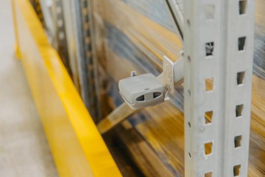 Un sensore grigio montato su una scaffalatura metallica da magazzino.