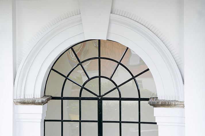White architectural archway with bird spikes over an arched window with black grilles.